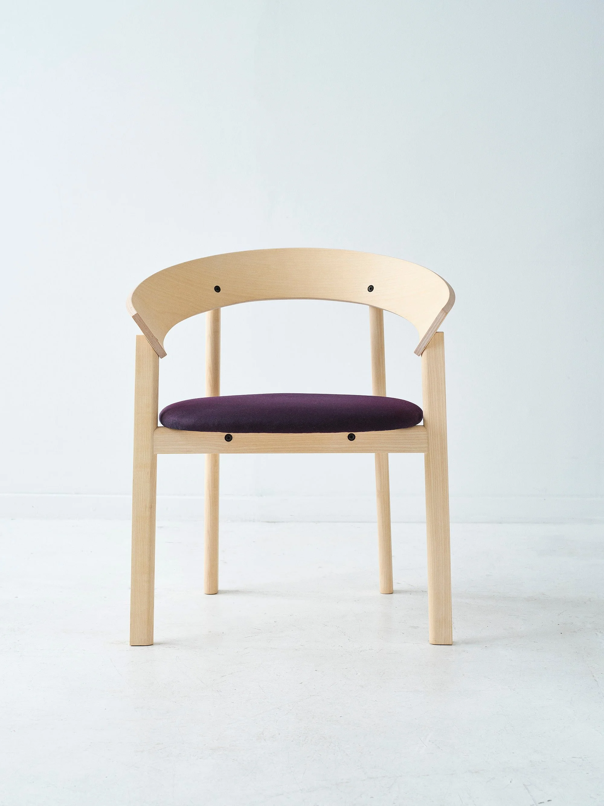Thérèse Chair / Therese stolen. A modern wooden chair with a dark purple cushion seat, set against a plain light background. For We Shelter by Mark de Vos Dalhoum. Danmarks næste klassiker 2026