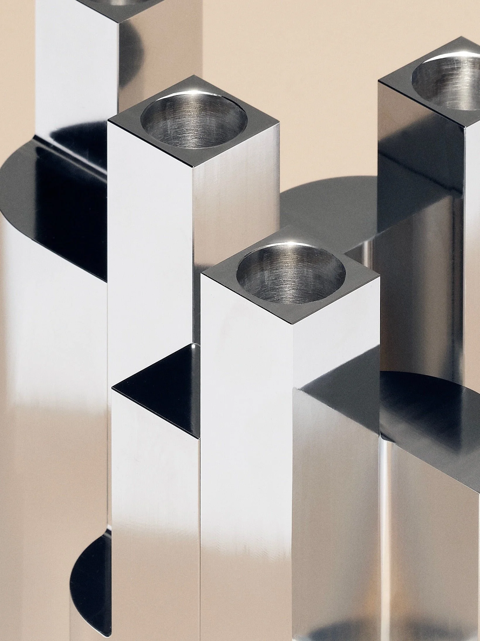 Closeup of minimalist aluminium candle holders  by Mark de Vos Dalhoum. hollow tops arranged on a reflective surface.