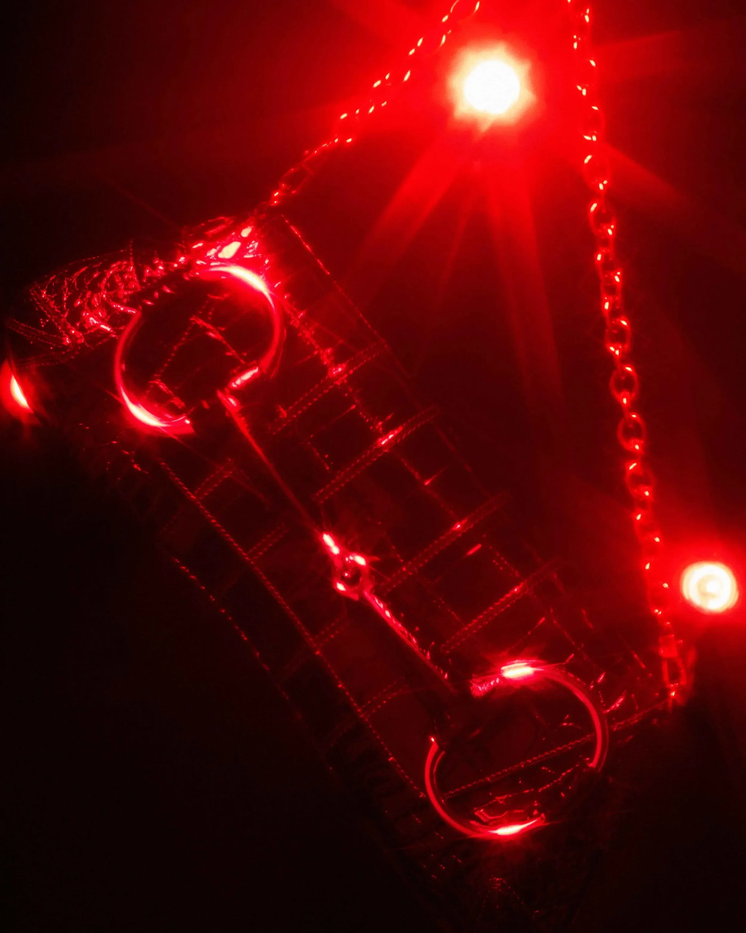 Fotografia still life editoriale per DNA Magazine centrata su una borsa Gucci con dettaglio morsetto (Horsebit) e tracolla a catena, immersa in un'atmosfera drammatica in luce rossa con riflessi e flare luminosi.