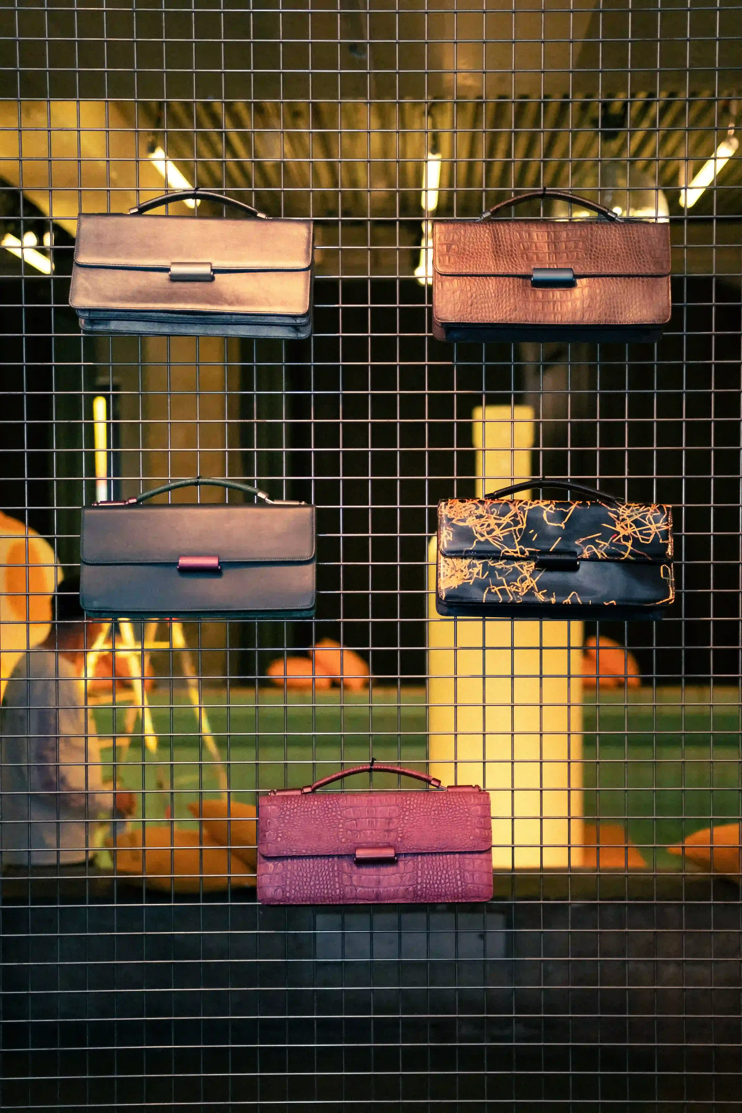 Esposizione d'archivio di borse in pelle Mandarina Duck sospese su una griglia metallica industriale, esempio di set design espositivo minimal per l'evento a Berlino.