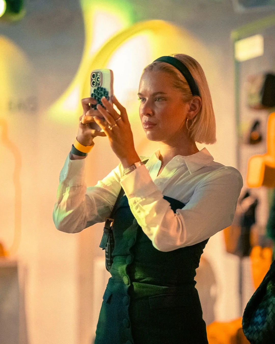Ospite dell'evento Mandarina Duck a Berlino mentre scatta una fotografia con lo smartphone, immersa nell'atmosfera e nei giochi di luce warm-toned dell'allestimento scenografico