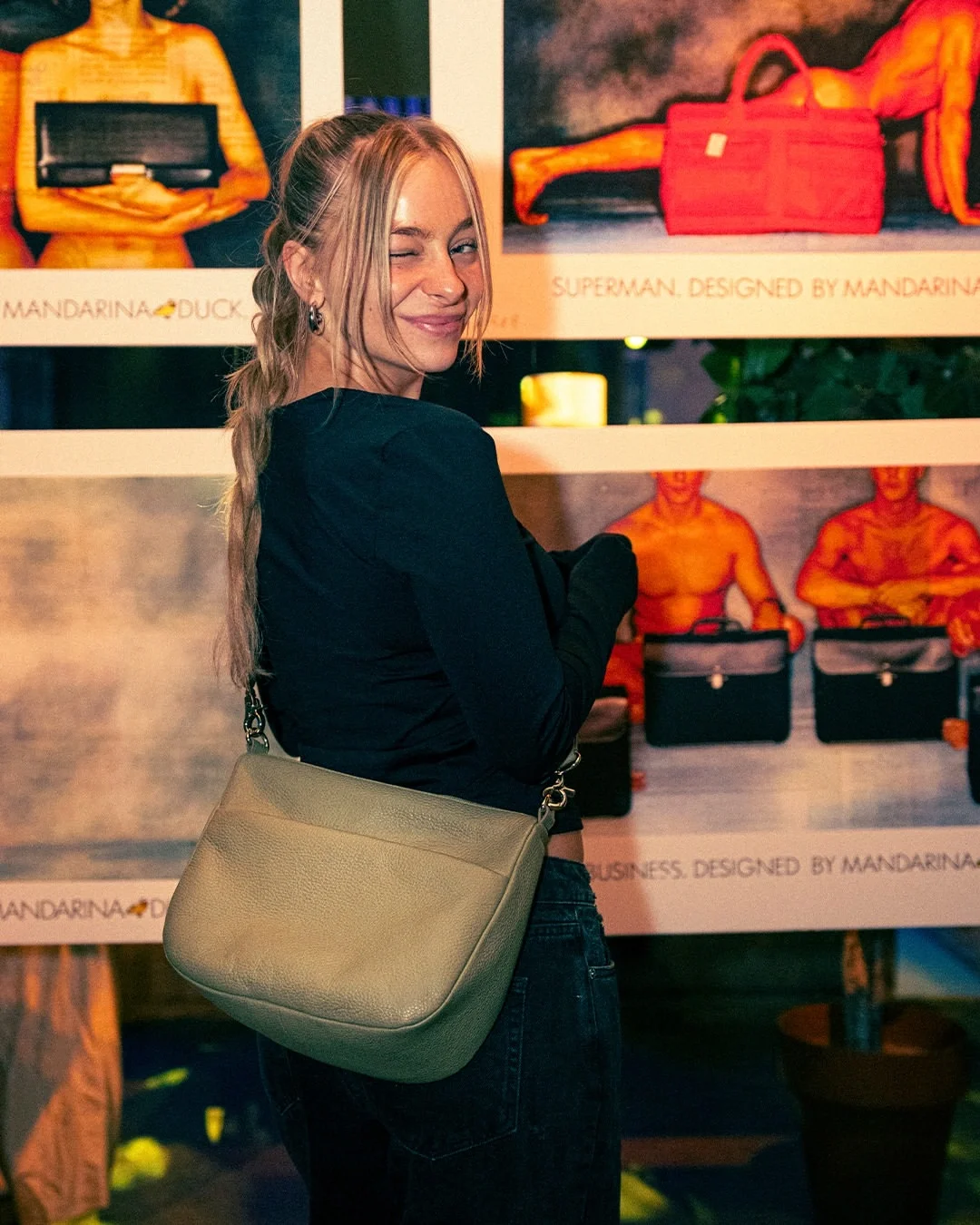 Modella indossa una borsa a tracolla in pelle Mandarina Duck posando davanti alle immagini storiche dell'archivio del brand allestite per l'evento a Berlino