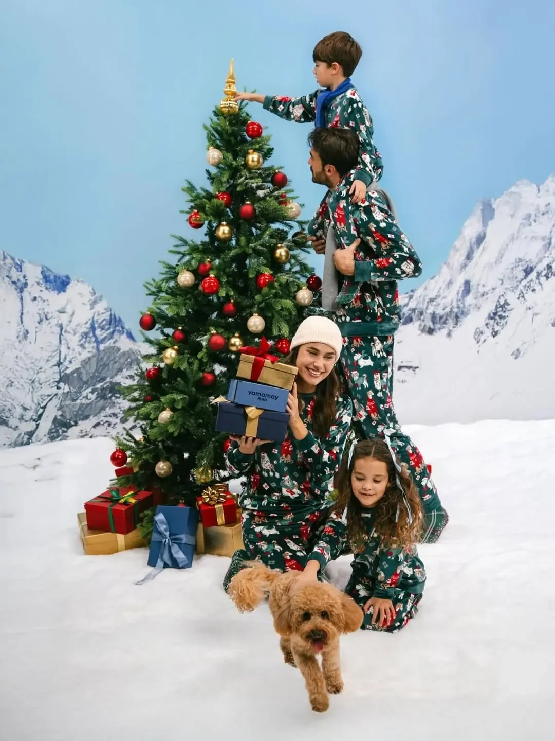 Foto di gruppo per la collezione natalizia Yamamay: famiglia con cane posa attorno all'albero di Natale all'aperto sulla neve, indossando pigiami verdi coordinati con stampe festive.