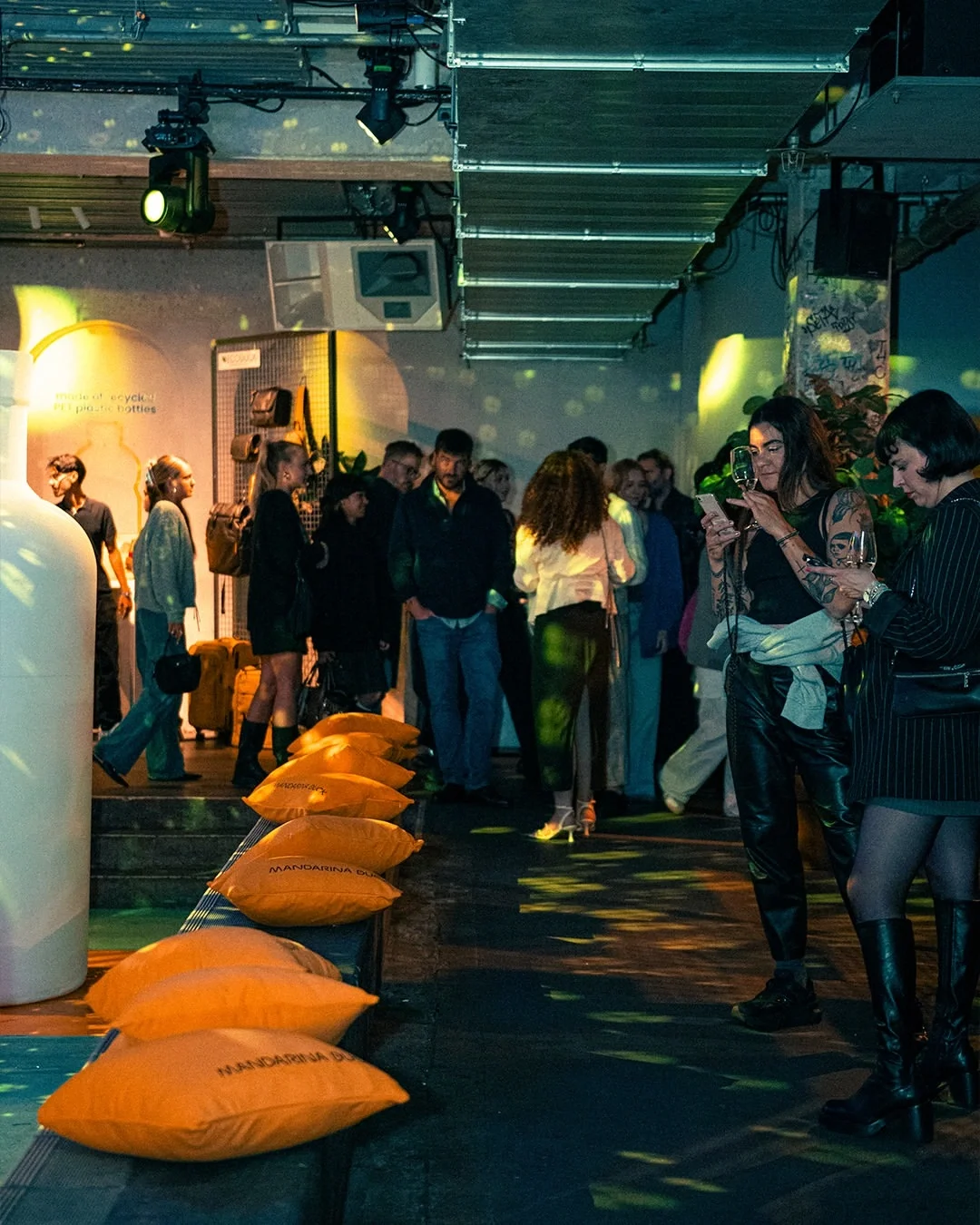Panoramica del party aziendale Mandarina Duck a Berlino con ospiti nell'area lounge, evidenziando il set design con cuscini iconici e proiezioni luminose d'atmosfera
