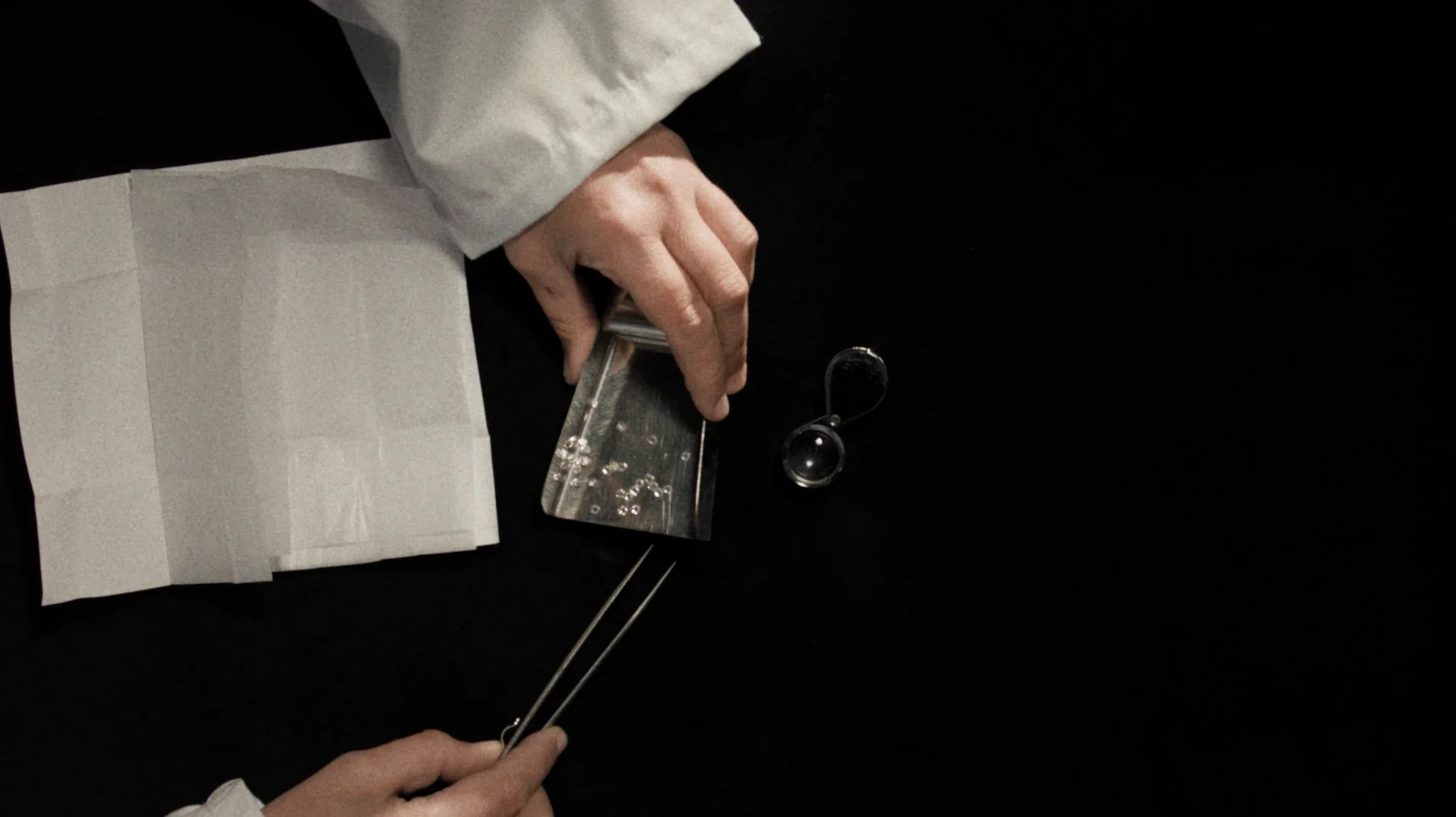 Inquadratura ravvicinata del gemmologo in camice bianco mentre raccoglie diamanti purissimi con una palette metallica da lavoro sul banco di laboratorio per Ralph Lauren.
