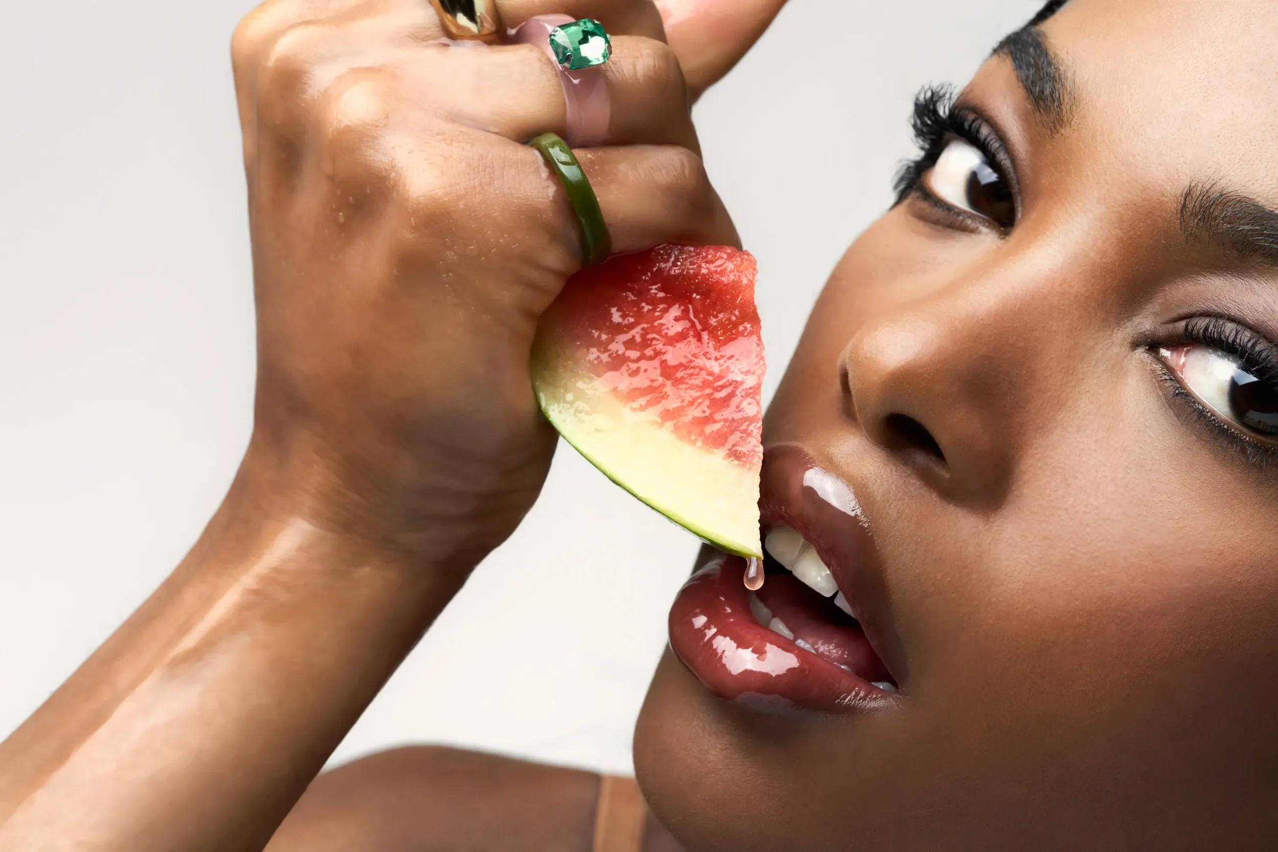 Fotografia beauty ed editoriale con modella che avvicina una fetta d'anguria succosa alle labbra truccate con gloss Pupa Pleasure Lips ultra brillante e gocce trasparenti.