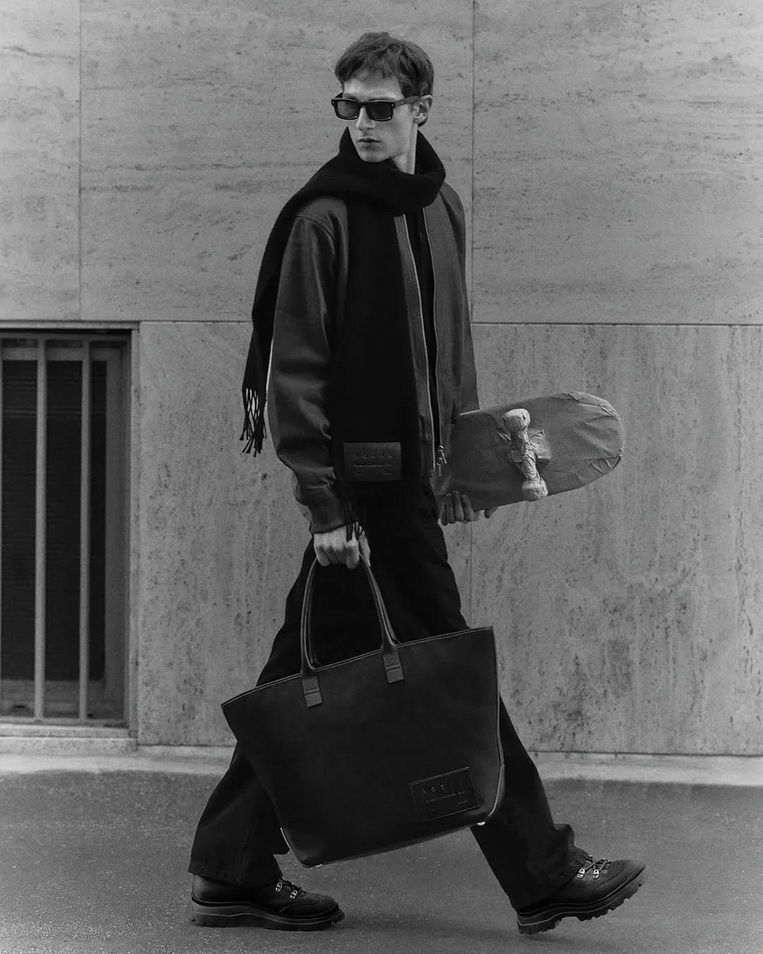 Direzione artistica e scenografia per la campagna pubblicitaria Hogan. Modello in total look scuro con tote bag in pelle e skateboard rivestito in carta artigianale.