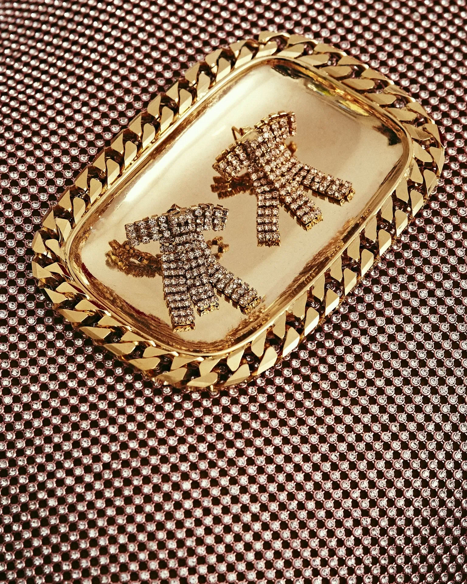 Dettaglio still life per la campagna Rosantica con orecchini a fiocco in cristalli disposti su un vassoietto dorato con bordo a catena.