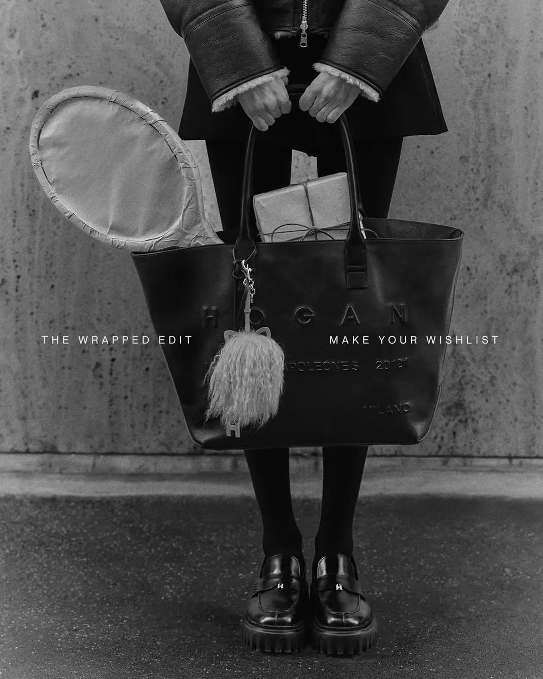 Inquadratura editoriale in bianco e nero per campagna ADV Hogan. Borsa shopper in pelle nera contenente una racchetta da tennis e un pacco regalo impacchettati in carta