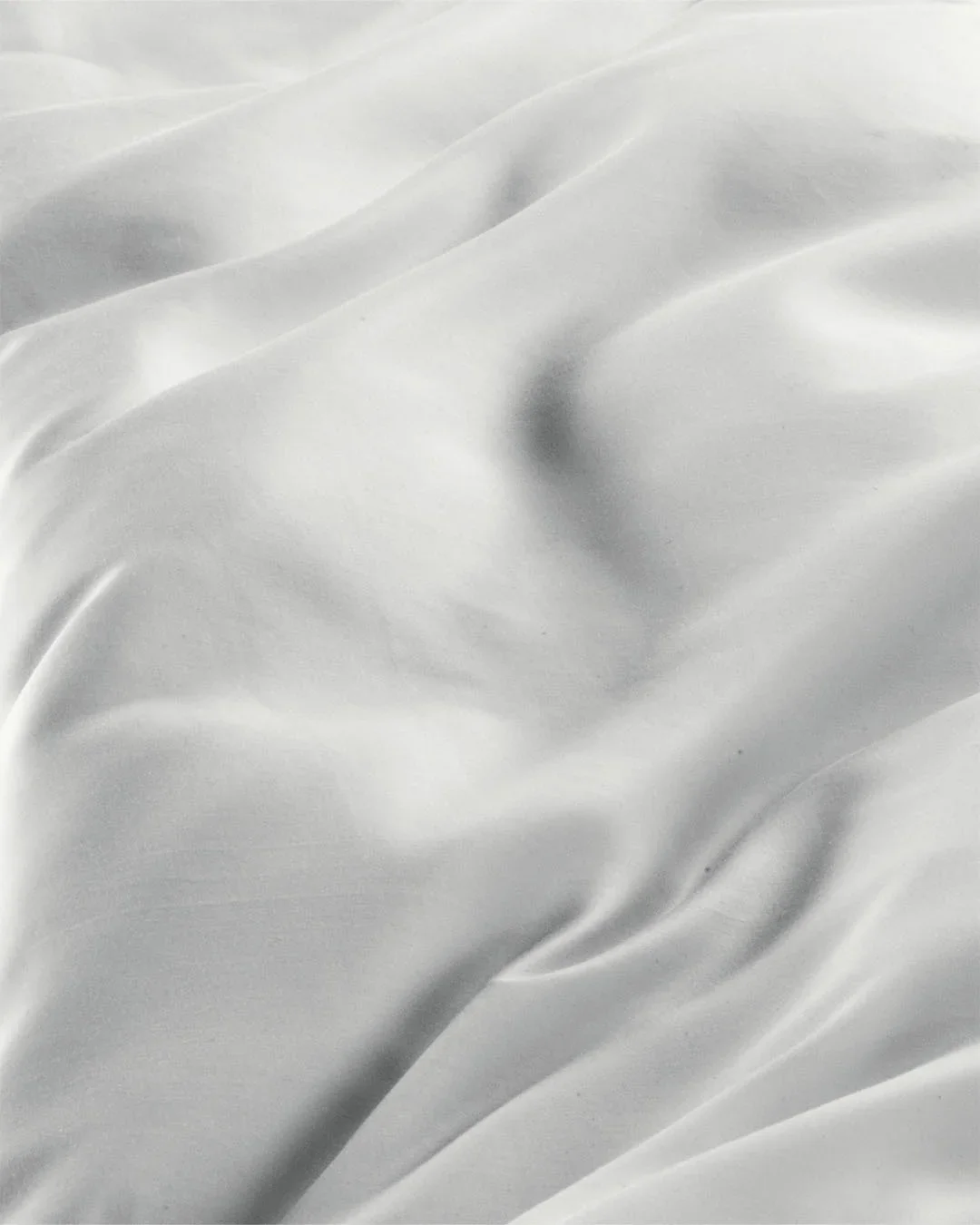 Dettaglio macro e fotografia still life di un draping in morbido tessuto di seta o raso bianco e argento, caratterizzato da pieghe fluide, rilievi cangianti e una luce morbida ed elegante