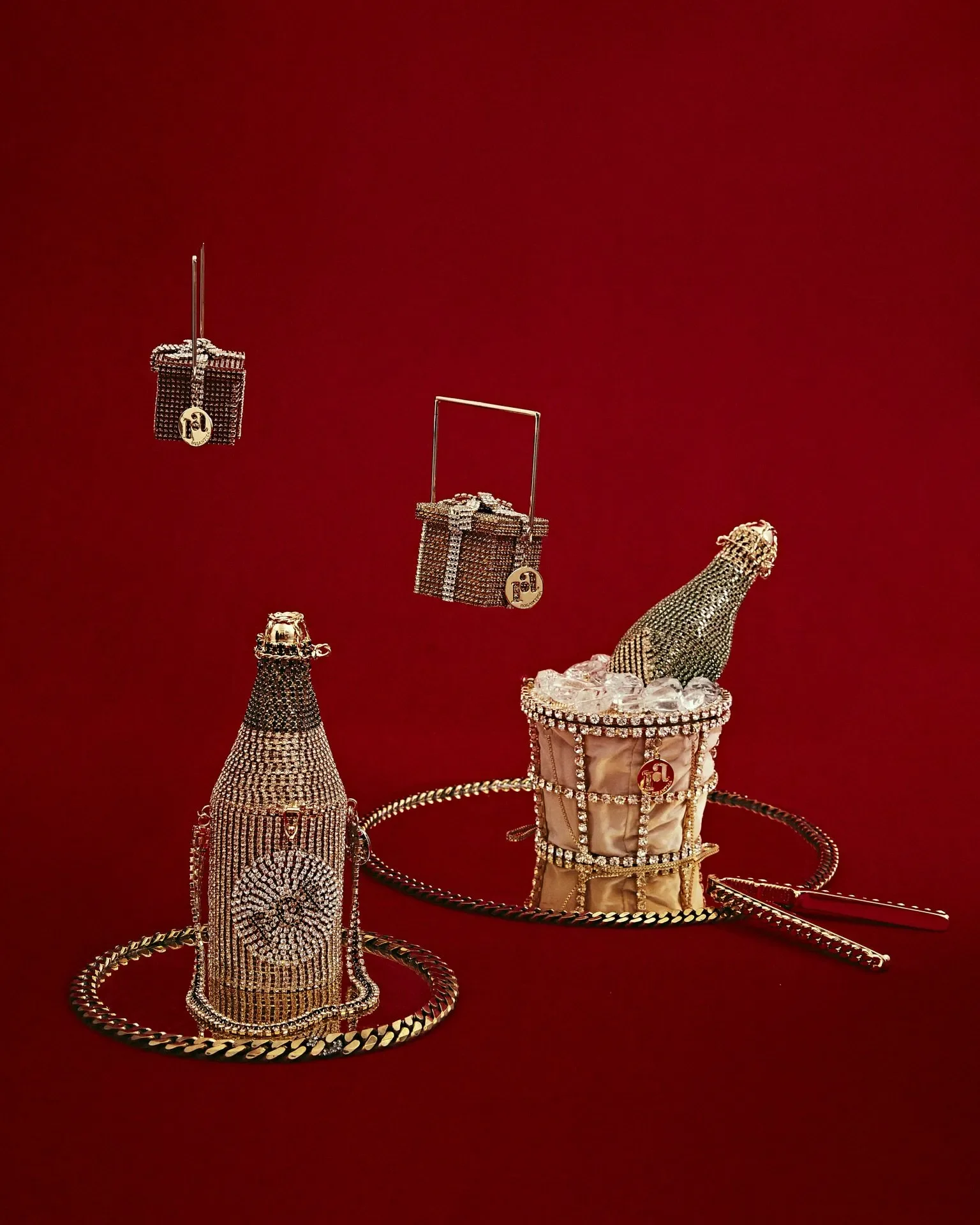 Fotografia still life per la campagna Rosantica con borse gioiello scultoree a forma di bottiglia di champagne, secchiello e pacchi regalo tempestati di cristalli.