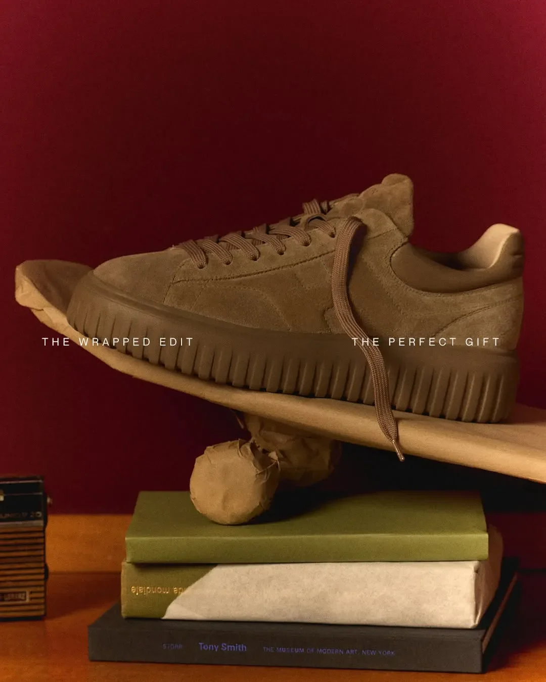 Set design e composizione in equilibrio per la campagna pubblicitaria Hogan 'The Wrapped Edit'. Sneaker in camoscio marrone adagiata su libri e oggetti impacchettati.