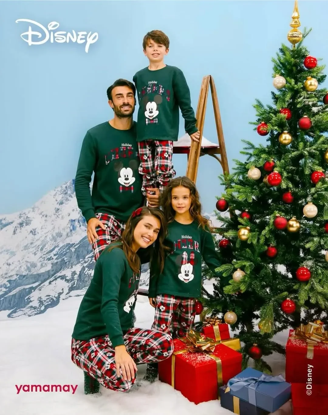 Foto di famiglia per la linea natalizia Disney Yamamay: genitori e bambini indossano pigiami verdi con grafica Mickey Mouse e pantaloni tartan, in posa accanto a un albero di Natale decorato con pacchi regalo.