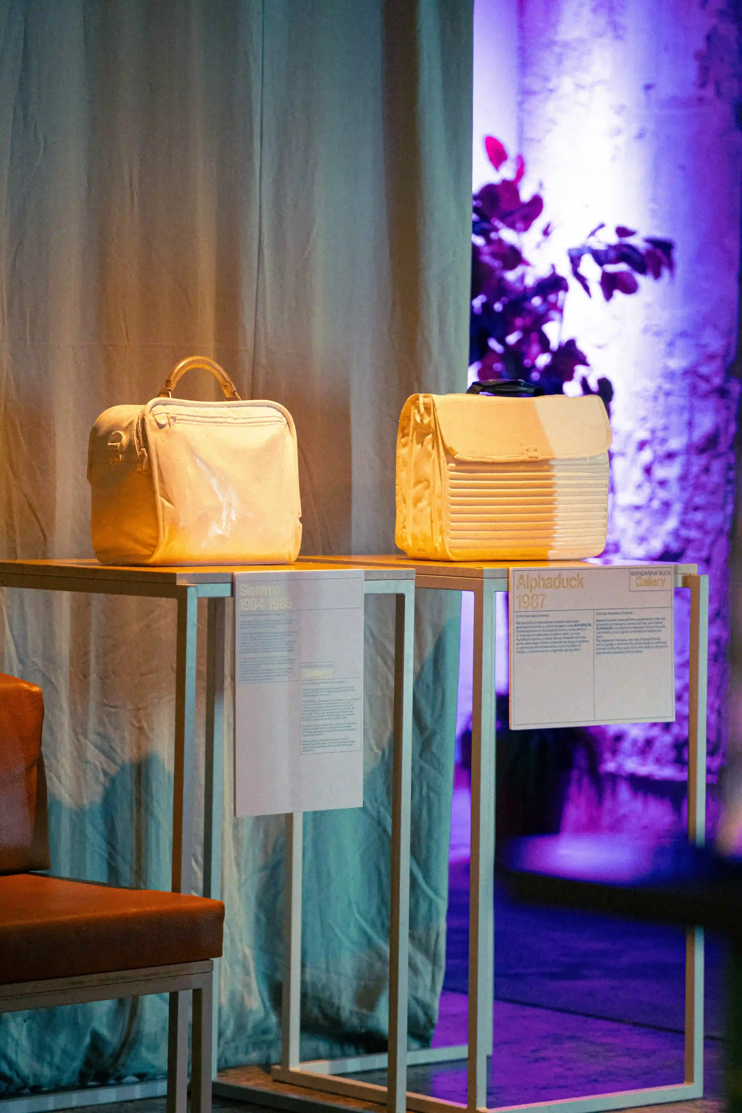 Display espositivo minimalista su strutture bianche con borse d'archivio storiche modelli Sistema e Alphaduck durante la mostra evento Mandarina Duck a Berlino.