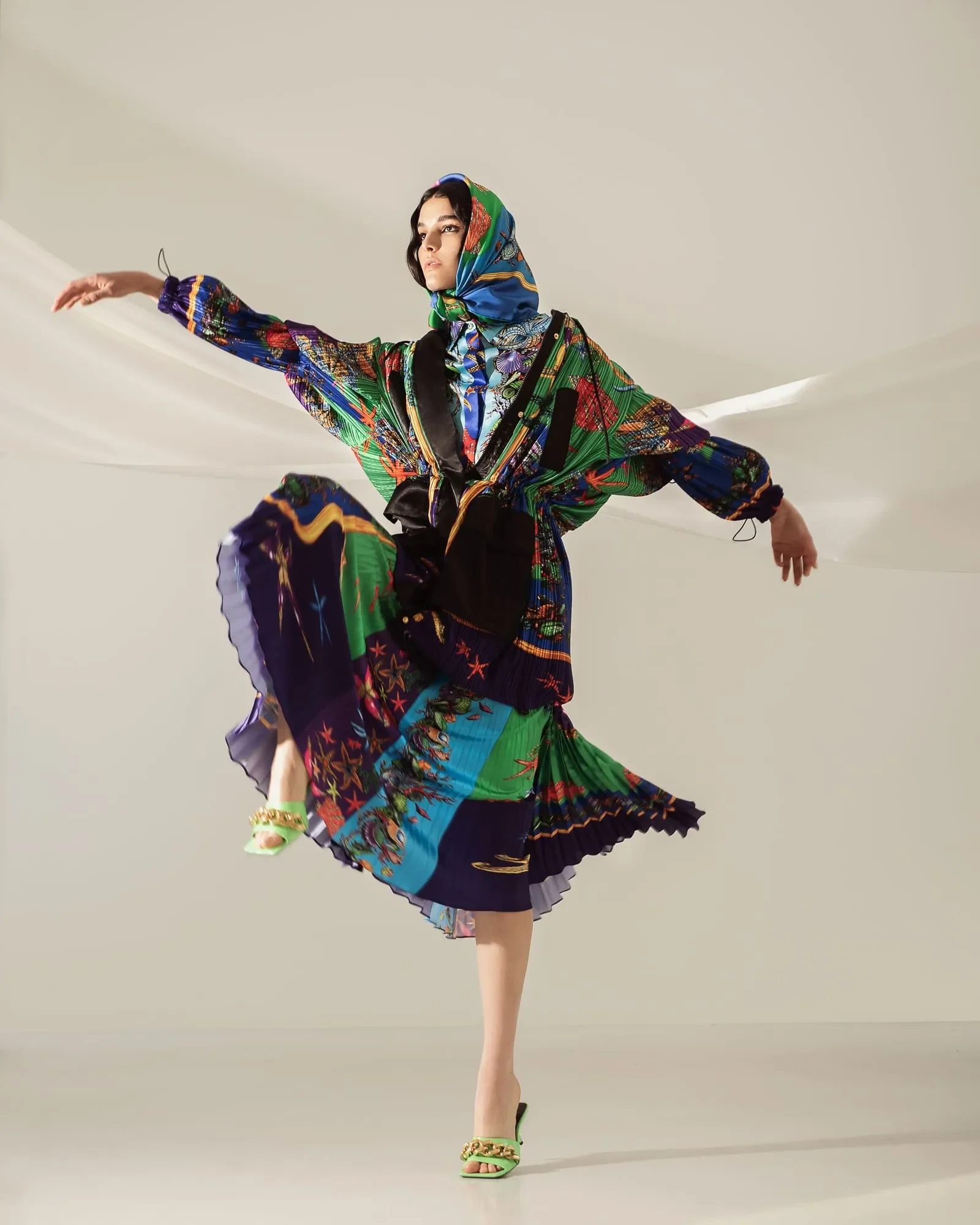 Posato dinamico della modella in abito plissettato con stampa multicolor marina, foulard coordinato e mules verdi con catena dorata.