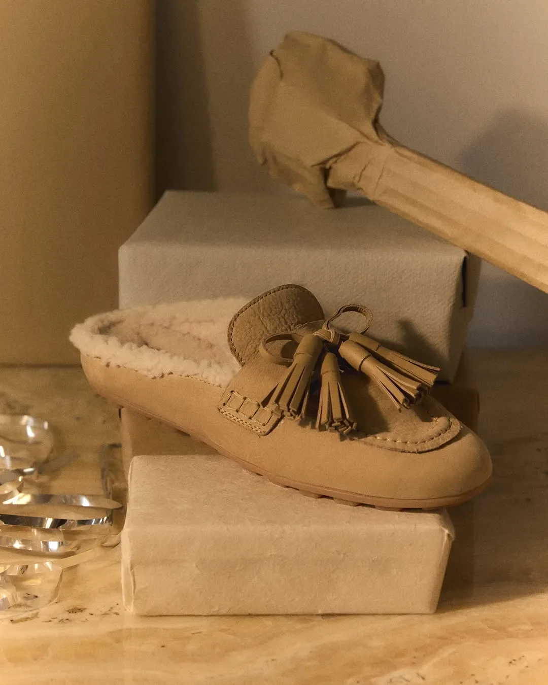 Set design e props styling per scatto still life Hogan. Sabot in camoscio beige con interno in shearling adagiato su pacchi regalo impacchettati in carta artigianale.