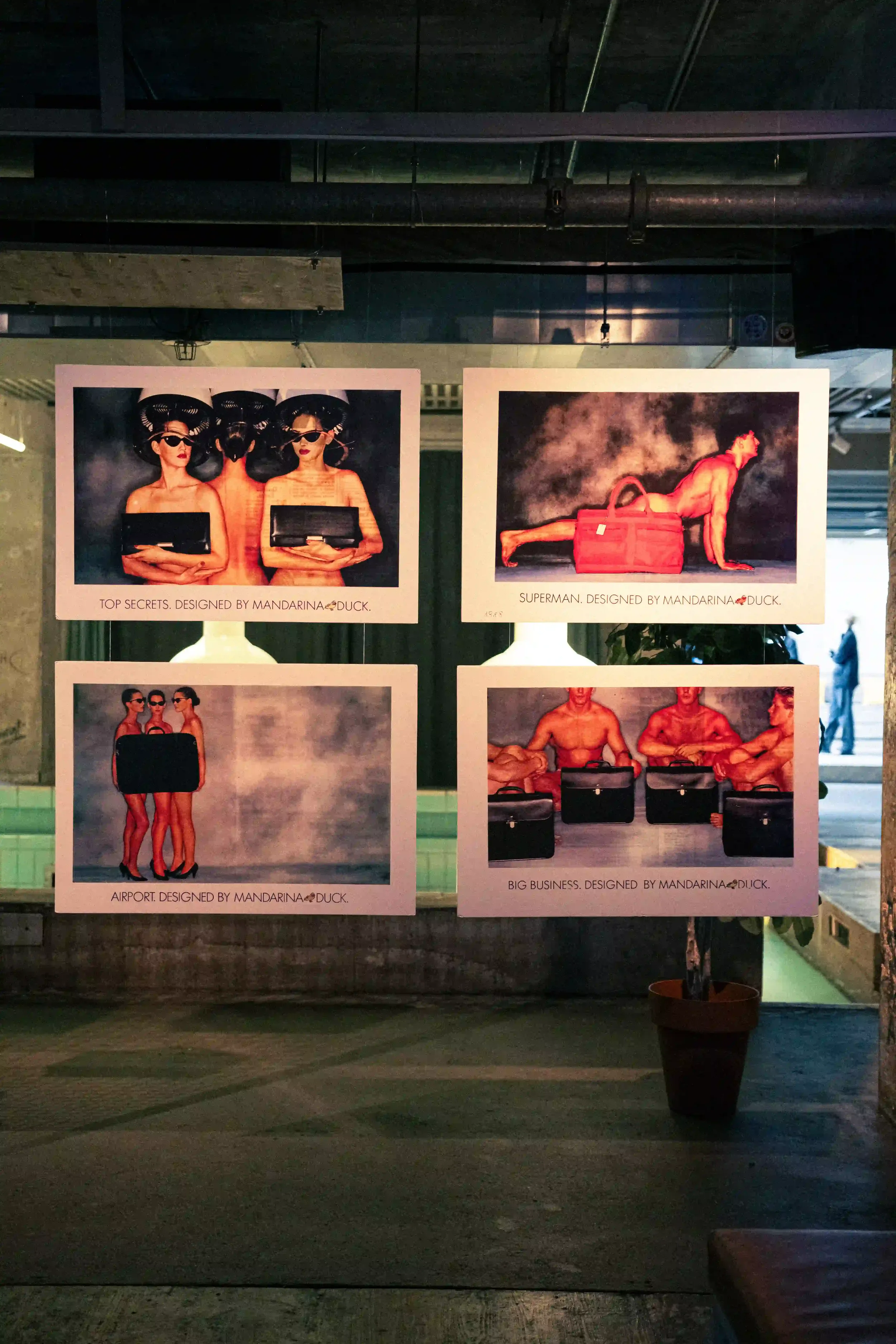 Stampe d'archivio delle campagne pubblicitarie storiche Mandarina Duck sospese per l'evento di Berlino. Set design espositivo minimal in una location dallo stile industriale.