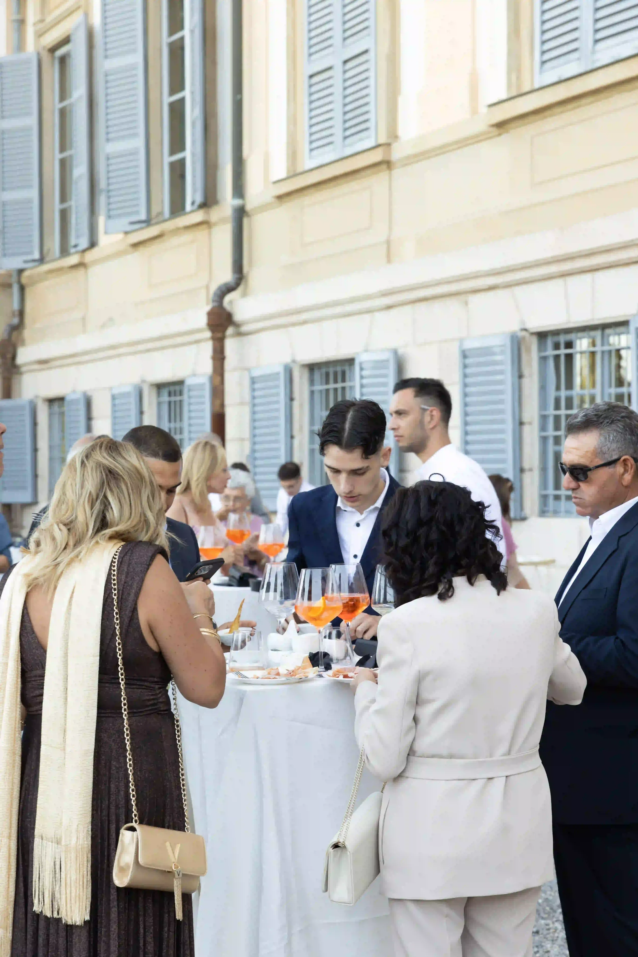 Ospiti durante l'aperitivo all'aperto di fronte alla facciata della villa storica, con tavoli alti, calici di spritz e atmosfera conviviale durante il ricevimento di nozze.