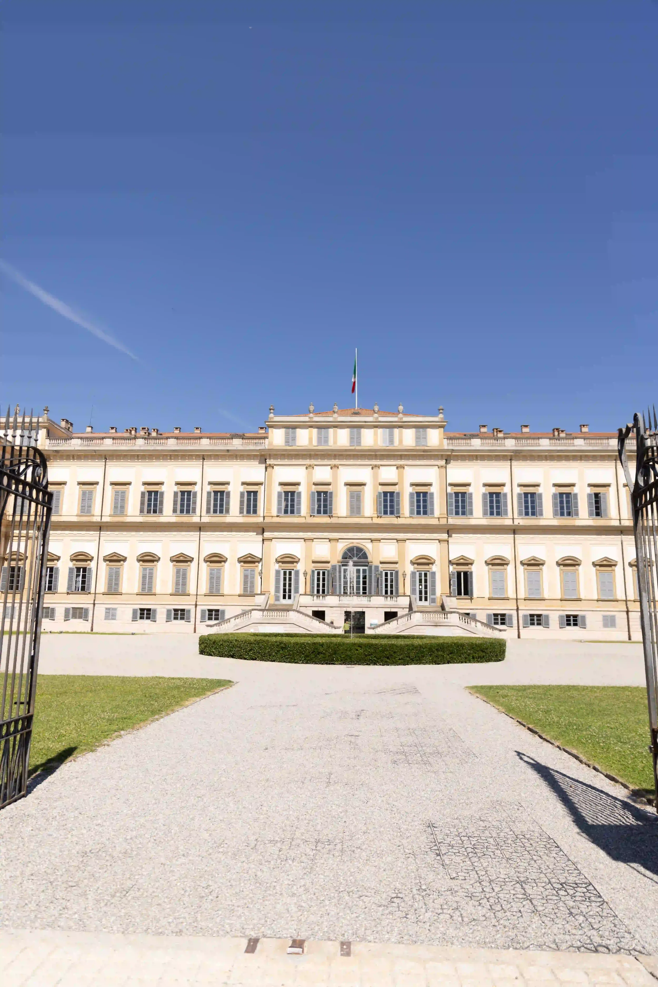 Facciata maestosa di una villa storica neoclassica con cancello in ferro battuto e viale in ghiaia, allestita come location esclusiva per un matrimonio ed evento privato.