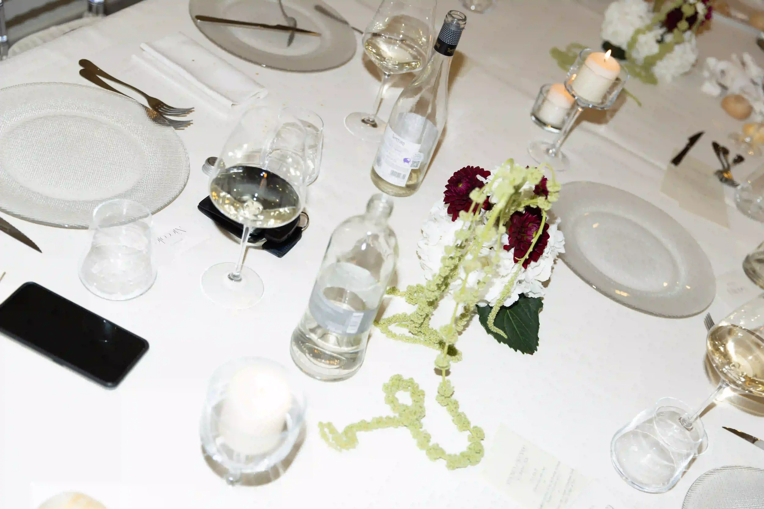 Dettaglio dall'alto della mise en place per la cena di nozze con centrotavola floreale di ortensie bianche, dalie bordeaux e amaranto ricadente, affiancato da calici e candele
