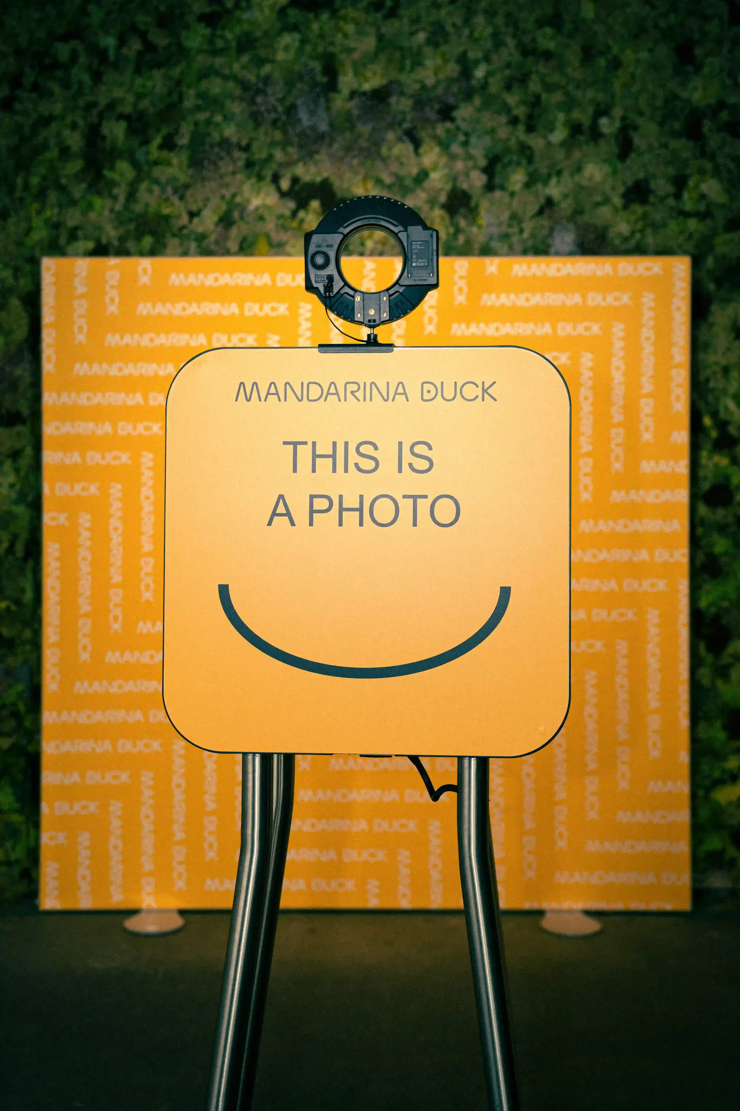 Postazione photobooth brandizzata per l'evento Mandarina Duck a Berlino con ring light, sfondo giallo pattern e cartello personalizzato 'THIS IS A PHOTO'