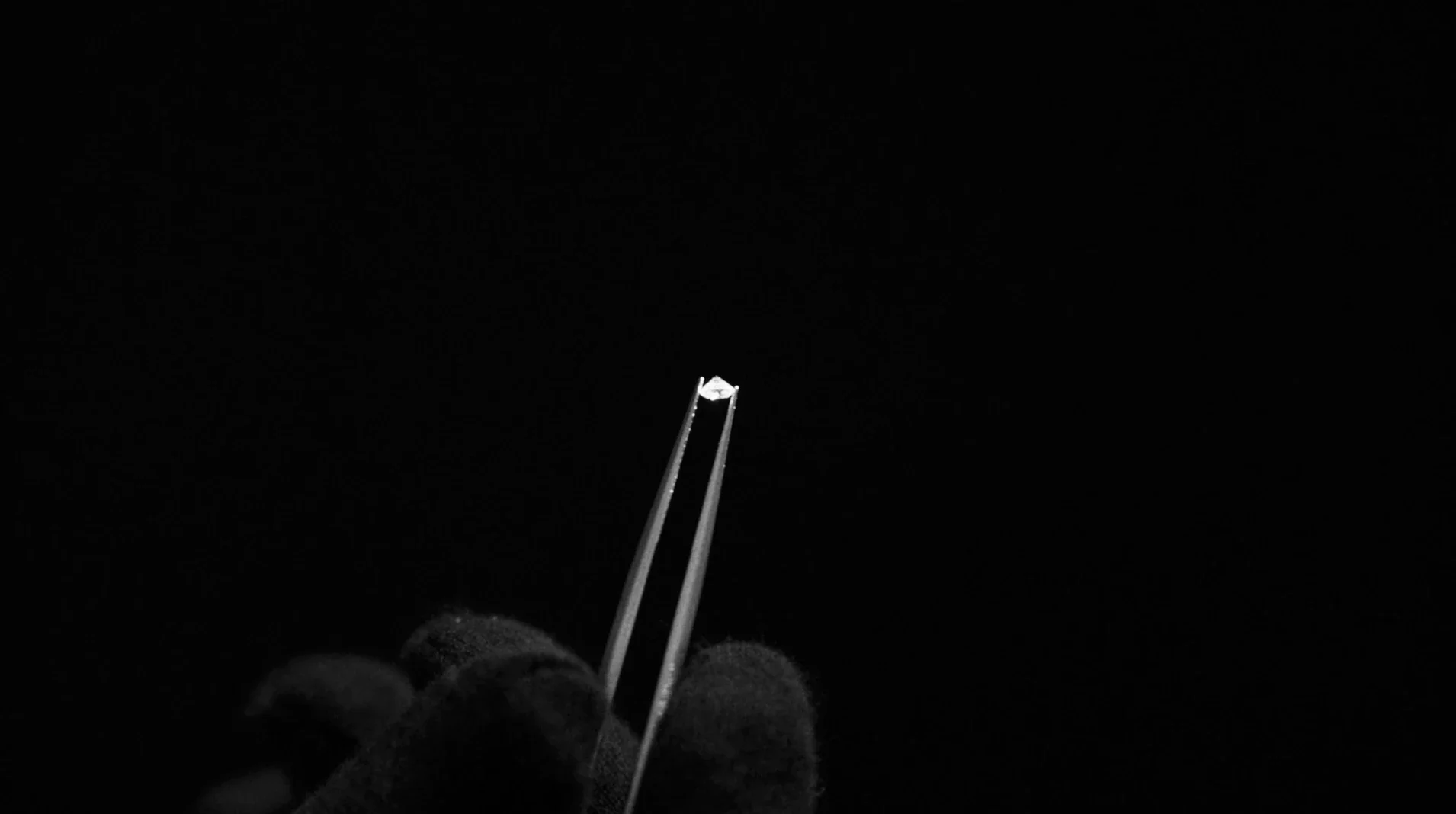 Primo piano drammatico di un singolo diamante brillante tenuto con pinzette da gemmologo su sfondo nero profondo per Ralph Lauren Fine Jewelry.