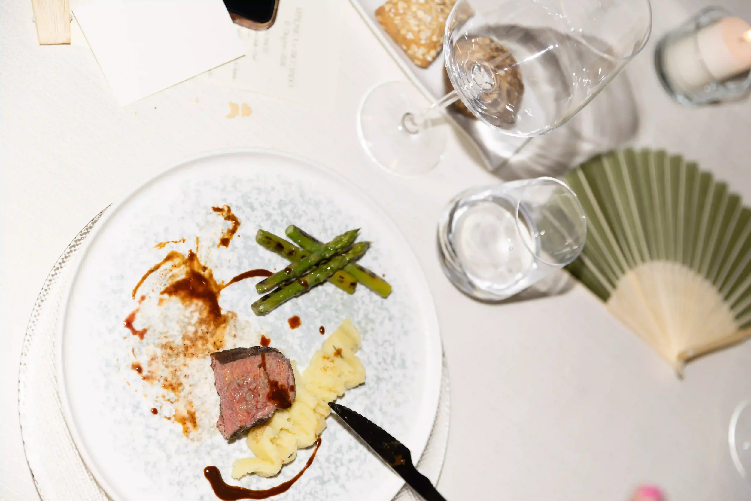 Vista dall'alto della portata principale per la cena di nozze: filetto di carne con riduzione di salsa, purè di patate e asparagi grigliati, accompagnato da ventaglio e menu.