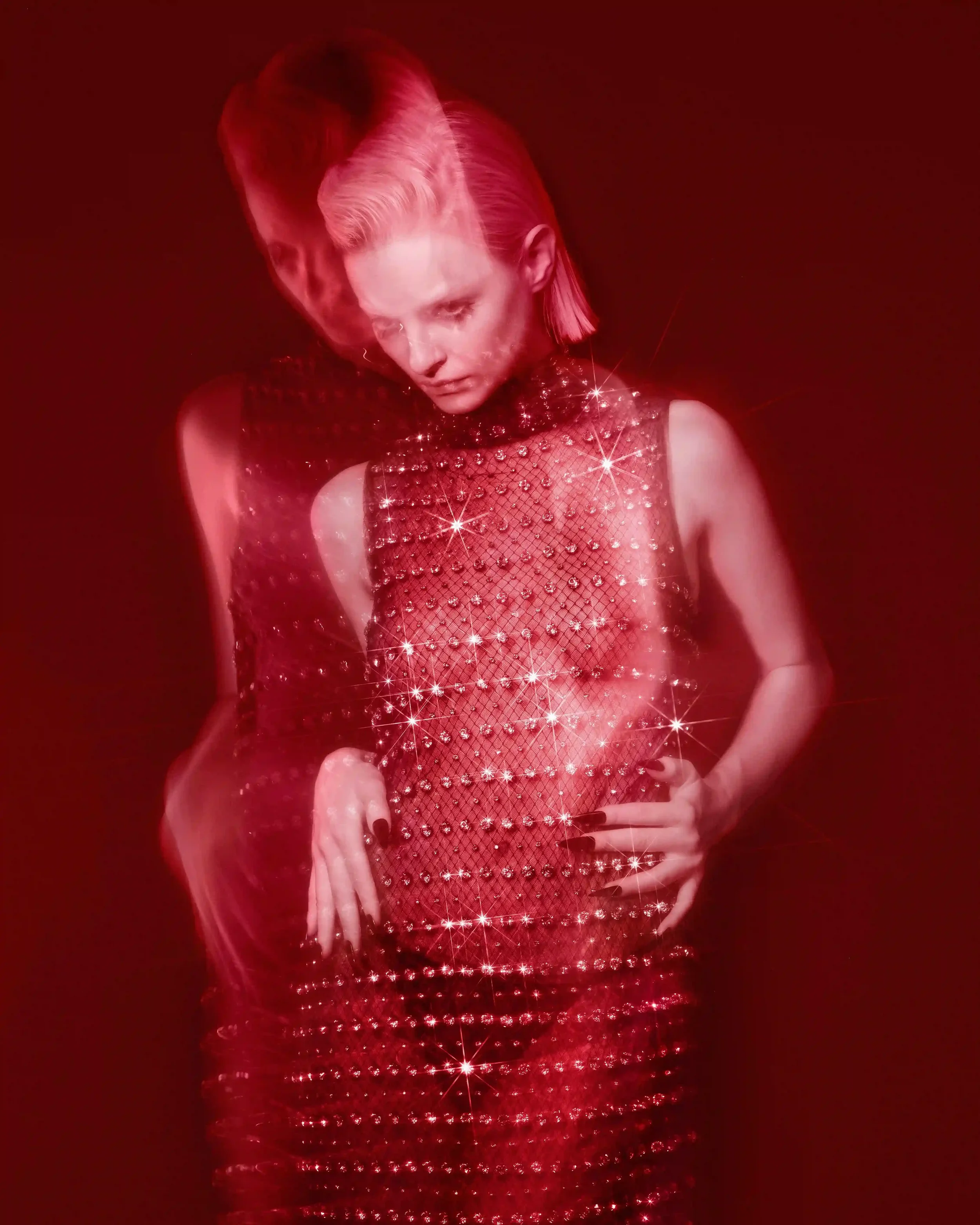 Scatto moda d'atmosfera con filtro rosso e giochi di luce per DNA Magazine e Gucci. Modella bionda con indosso un abito smanicato a rete semitrasparente interamente impreziosito da cristalli scintillanti.