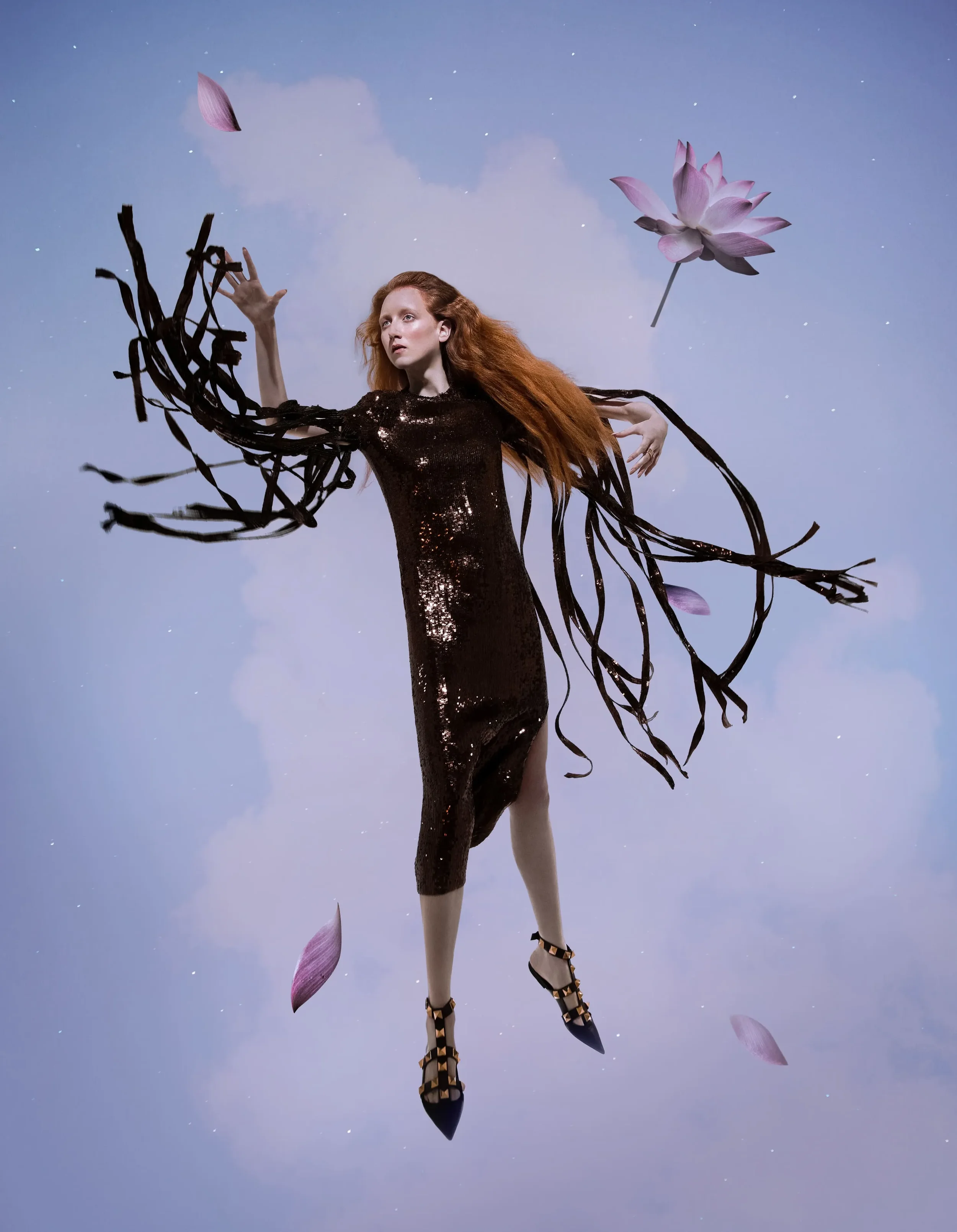 Fotografia concettuale per Vogue Portugal con modella sospesa nel cielo che indossa un abito di paillettes scure con lunghe frange sulle maniche, scarpe borchiate e petali di fior di loto galleggianti.