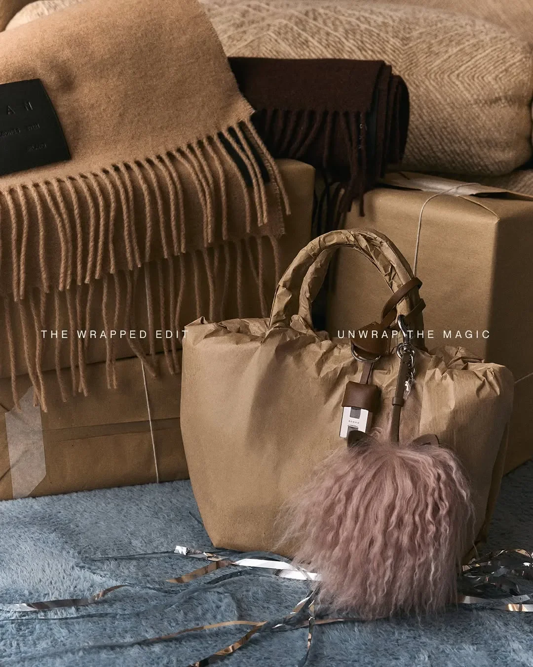 Props styling e set design per la campagna Hogan 'Unwrap the Magic'. Borsa scultura in carta kraft con charm in piuma rosa affiancata da sciarpe in lana frangiate e pacchi regalo.