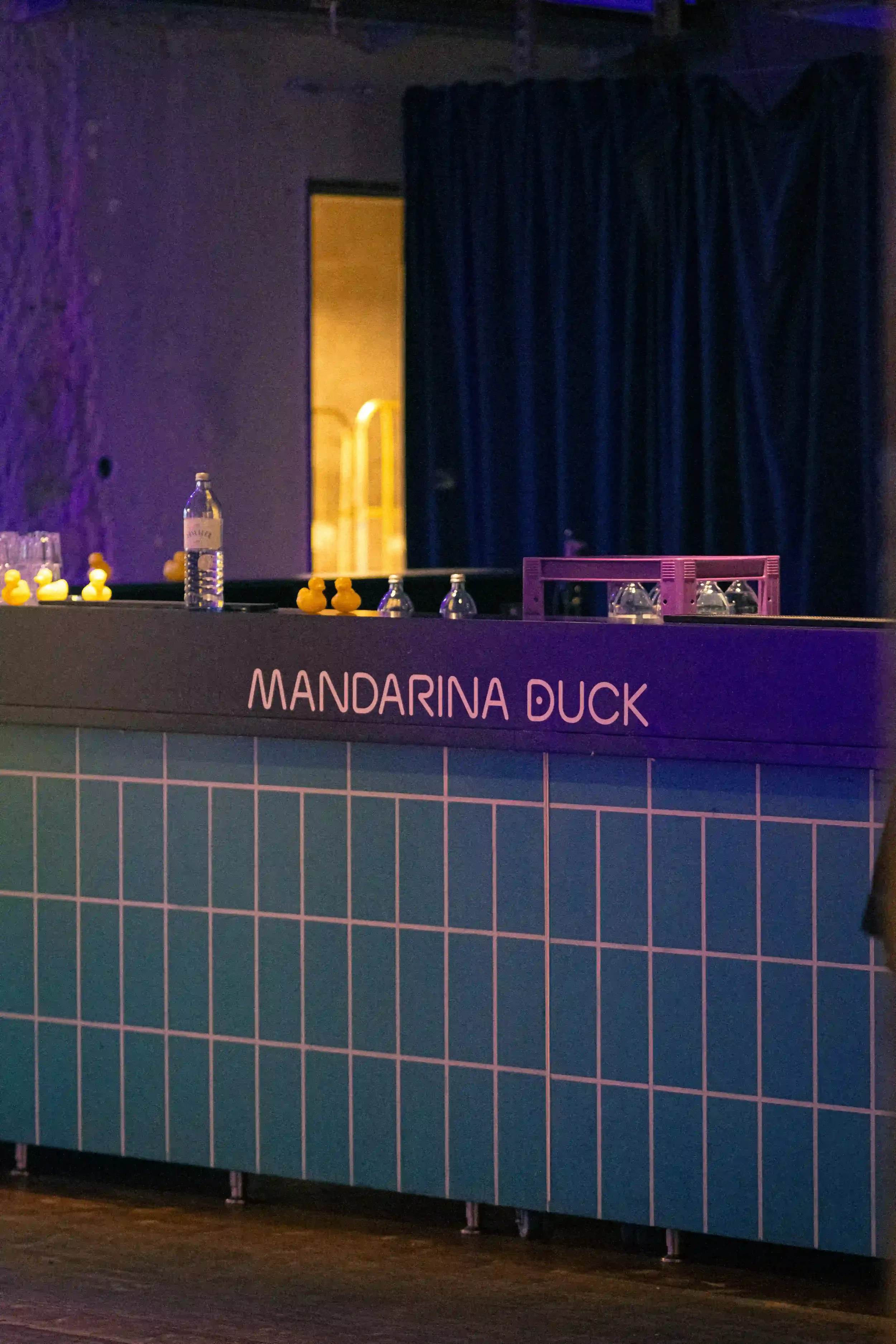 Dettaglio del bancone bar in piastrelle azzurre per l'evento Mandarina Duck a Berlino, allestito con l'iconica serie di paperelle gialle in gomma lungo la superficie