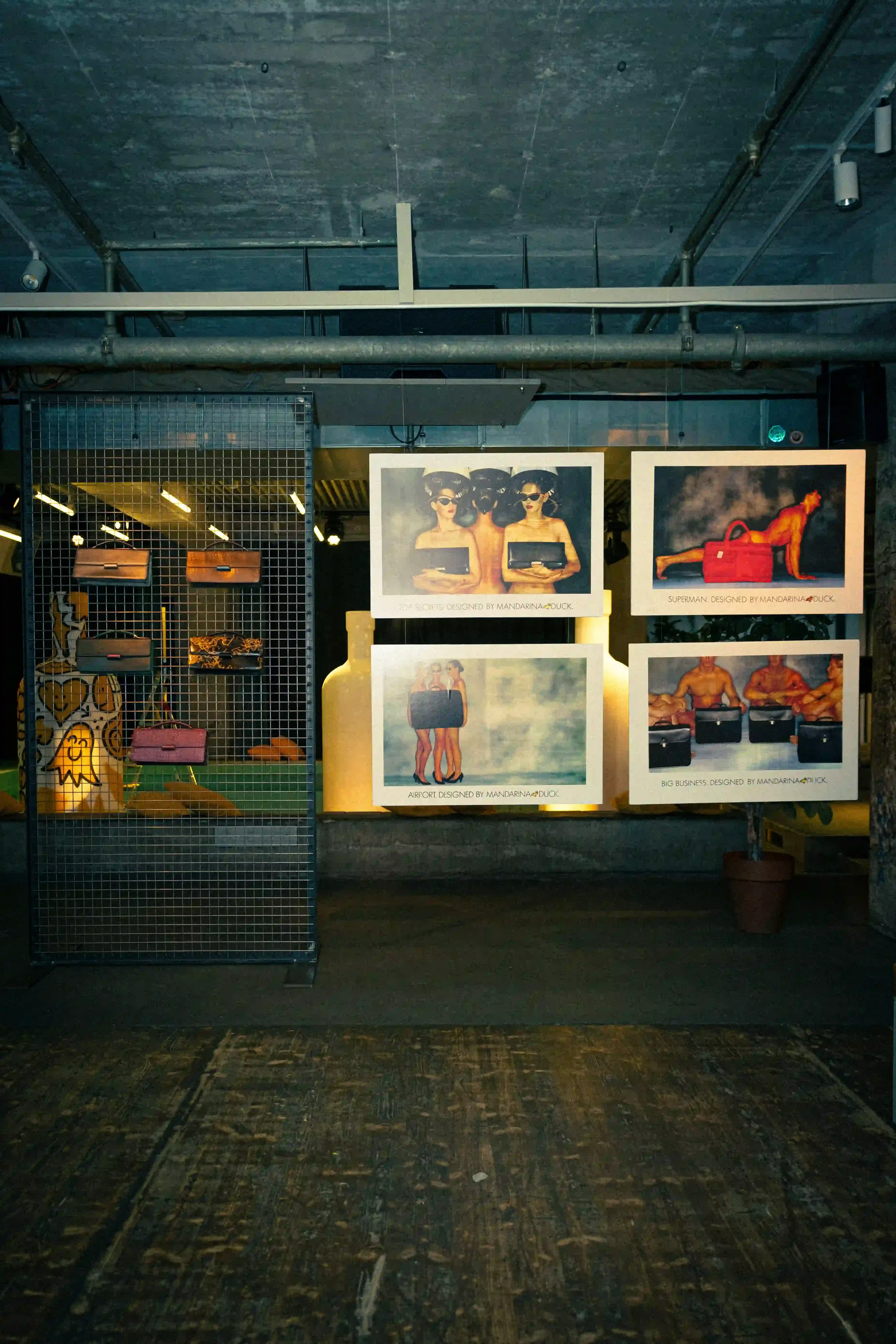 Allestimento espositivo d'archivio per Mandarina Duck a Berlino con poster pubblicitari storici sospesi e borse in pelle vintage presentate su una griglia metallica nera.