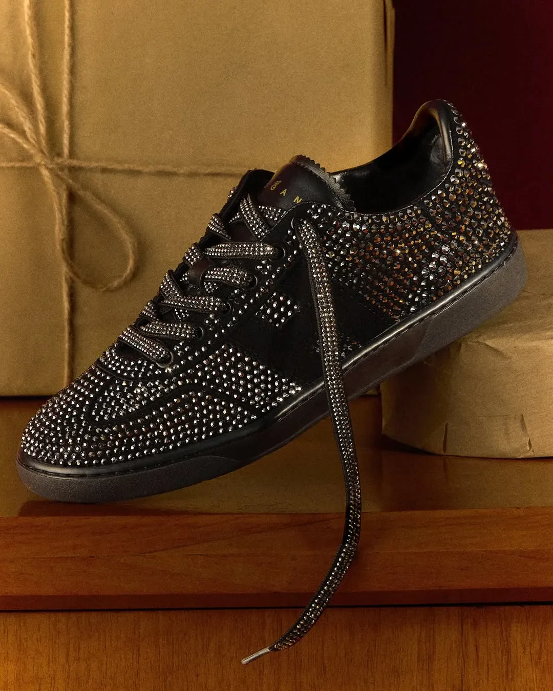Composizione still life e set design per la campagna Hogan. Dettaglio di sneaker nera ricoperta di cristalli brillanti su piano in legno con pacchi regalo di sfondo