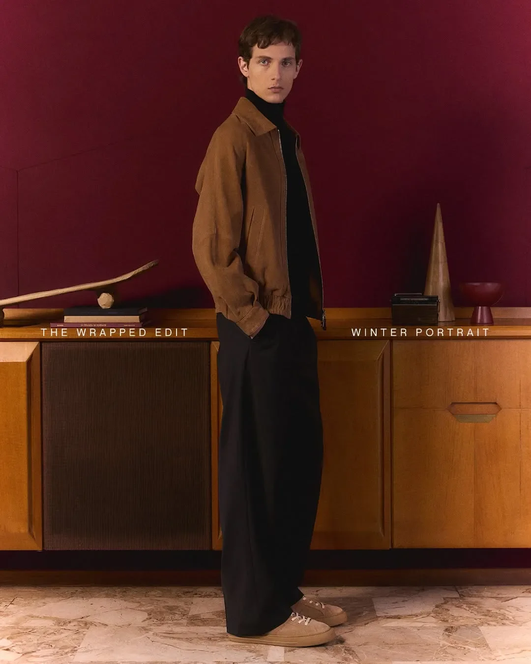 Scenografia d'interni e set design per la campagna Hogan 'Winter Portrait'. Modello maschile accanto a credenza vintage con props artistici impacchettati in carta.