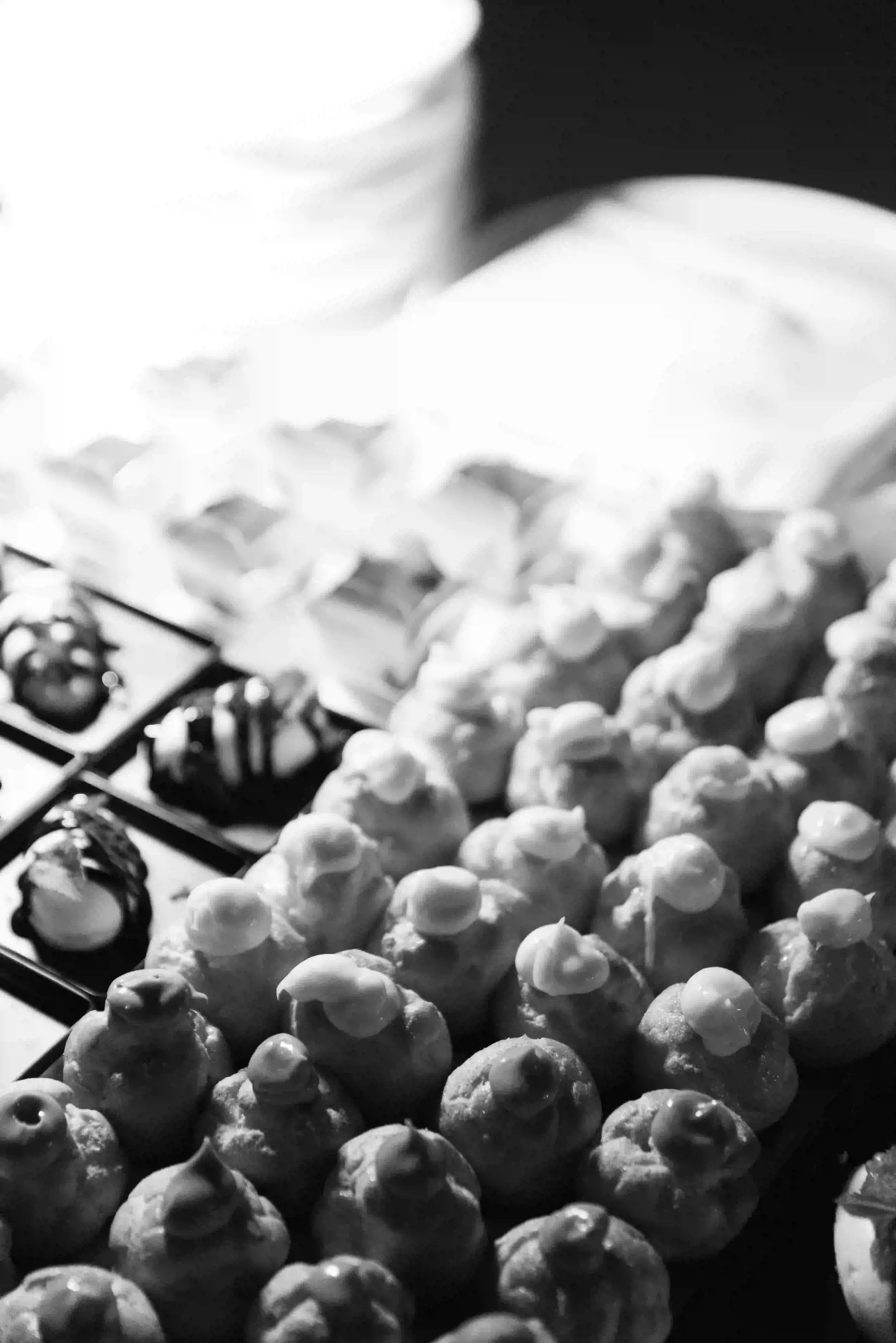 Inquadratura ravvicinata in bianco e nero del buffet dei dolci durante il ricevimento di nozze, con un'elegante selezione di bignè alla crema e piccola pasticceria gourmet.