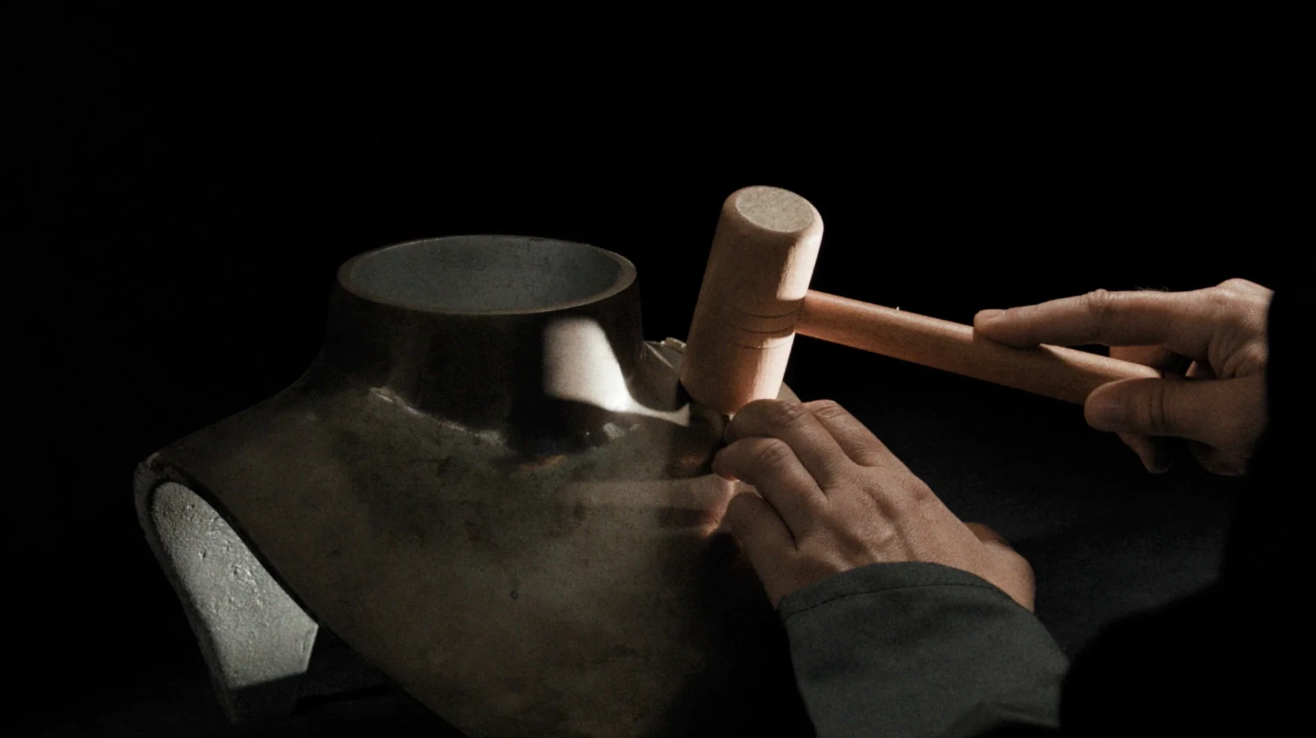 Mani artigiane che utilizzano un martello in legno per modellare la struttura di una collana su un busto in metallo per la gioielleria Ralph Lauren