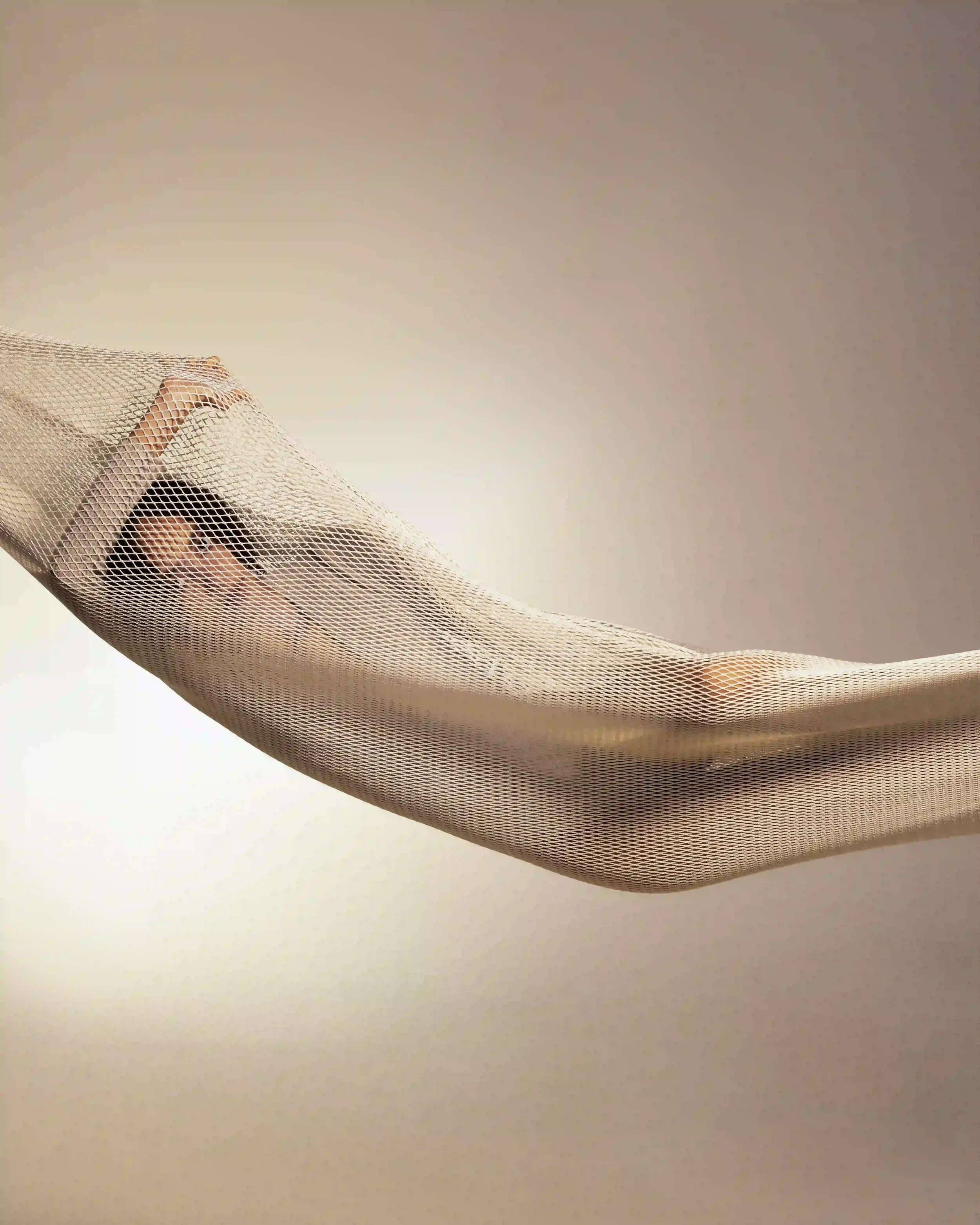 Props styling e installazione concettuale per editorial moda Laneus: modella avvolta all'interno di una struttura a rete traforata sospesa su sfondo neutro illuminato.