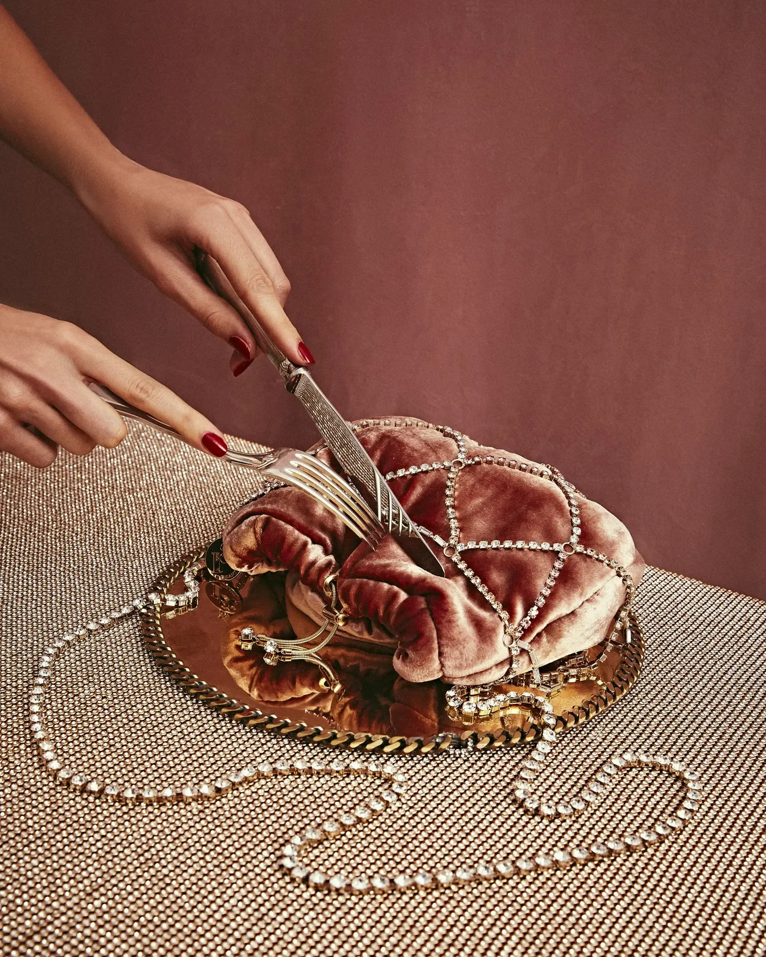 otografia still life della campagna Rosantica con mani che utilizzano posate d'argento su una borsa in velluto rosa rivestita da una rete di cristalli.