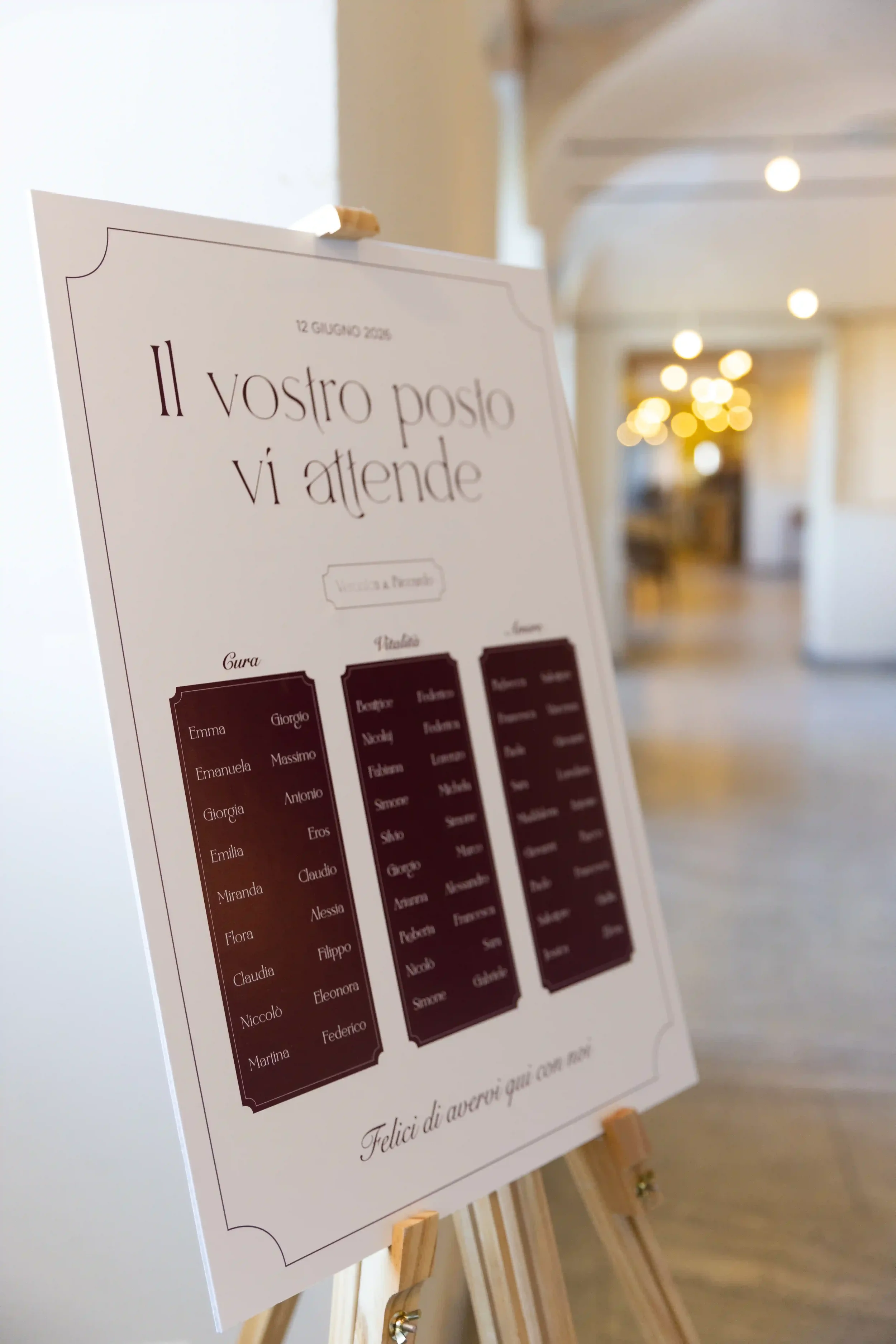 Tableau de mariage su cavalletto in legno con grafica elegante, intestazione 'Il vostro posto vi attende' e schede bordeaux indicanti l'organizzazione dei tavoli per la cena di nozze.