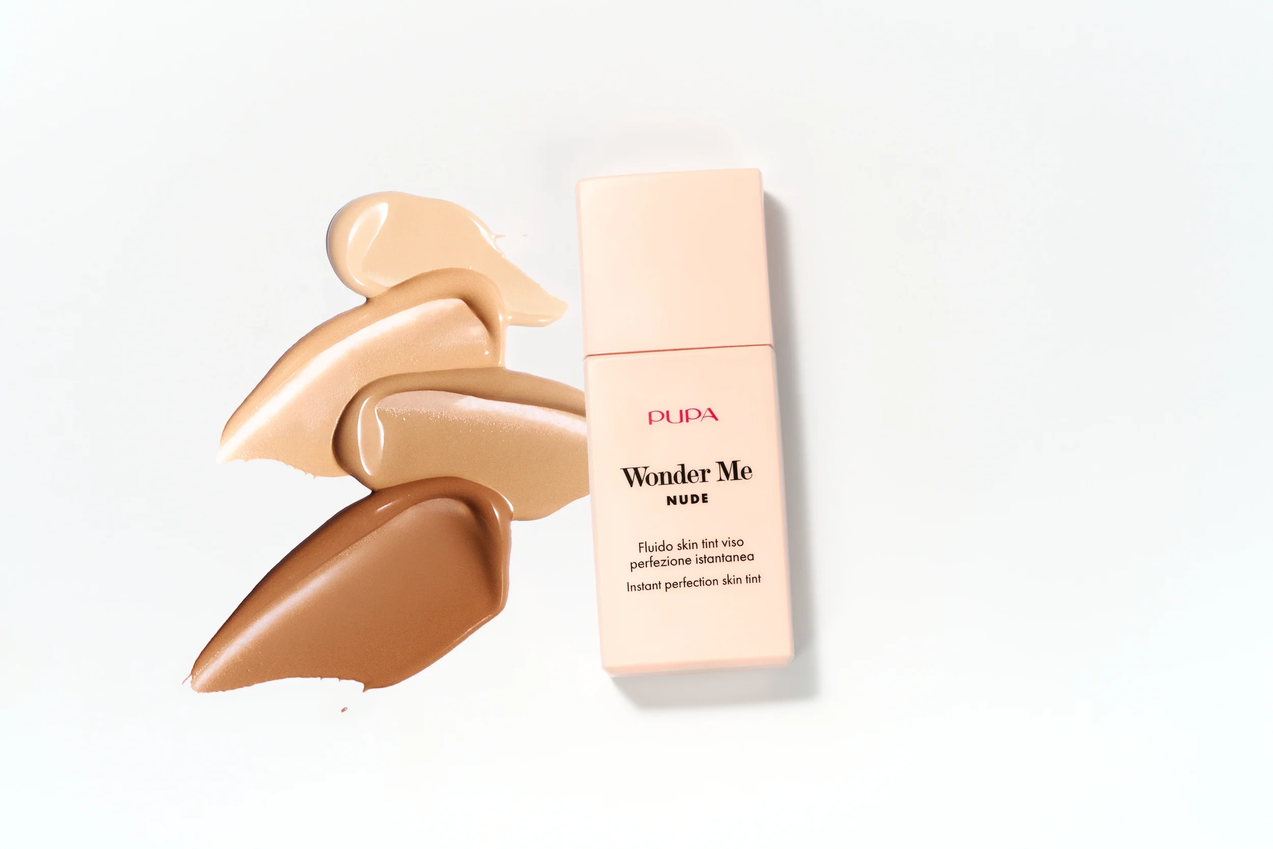 Fotografia still life del fluido skin tint Pupa Wonder Me Nude affiancato da quattro swatch di texture cremosa in differenti sfumature di incarnato su sfondo bianco essenziale.