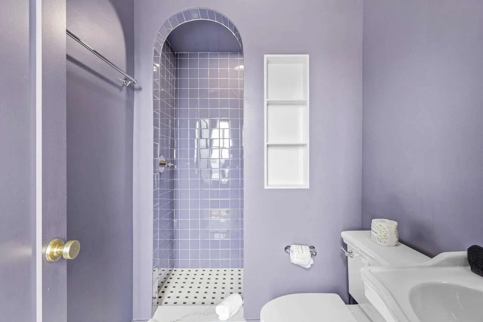 The Amethyst Chamber Bathroom featuring lilac tiles, a toilet, a pedestal sink, a shower, and a wall-mounted cabinet.