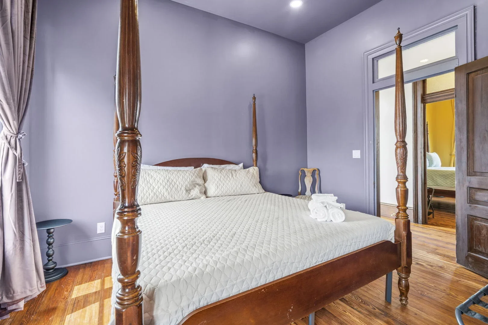 The Amethyst Chamber with a wooden four-poster queen sized bed, a small side table, and armoire