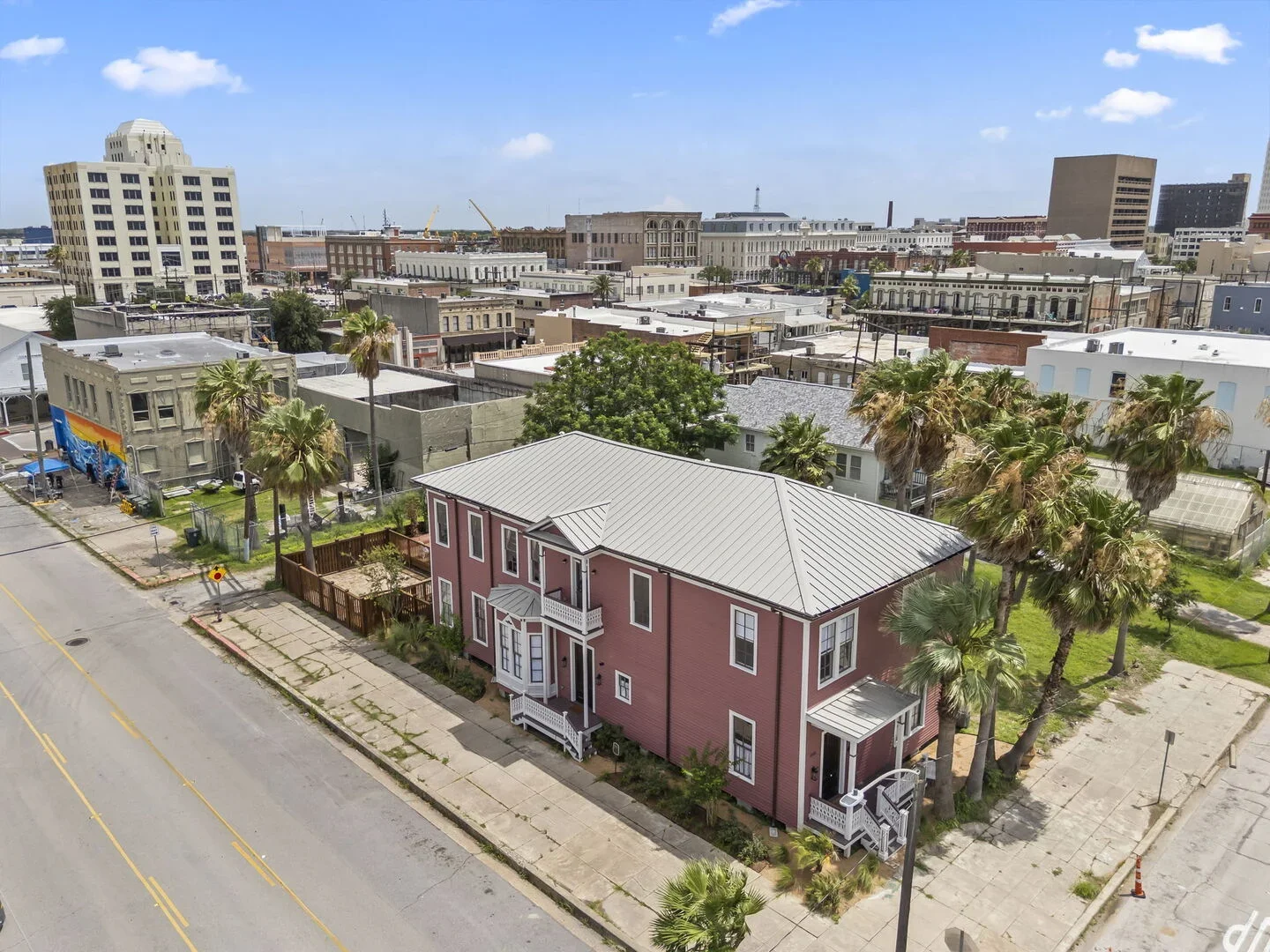 The pink two-story restored 1886 Mollie Walters House surrounded by palm trees in an urban neighborhood with various buildings and a cloudy sky.