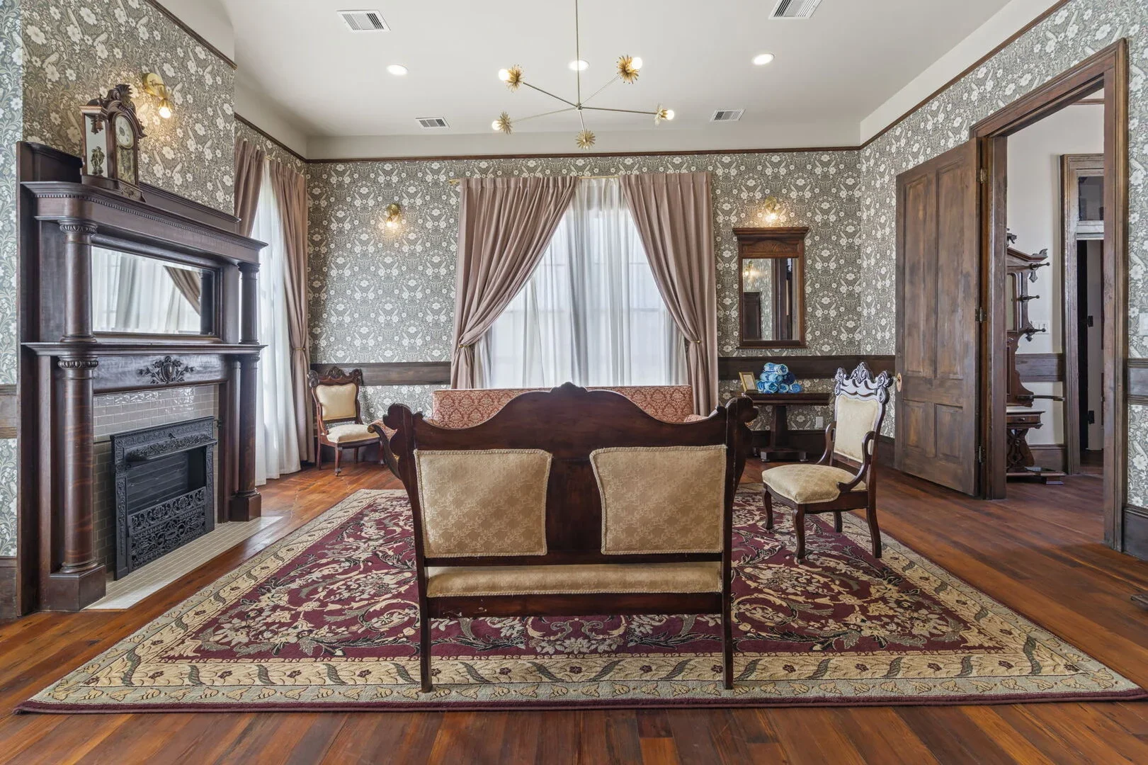 Historic Victorian Scarlet Parlor inside the Mollie Walters House in downtown Galveston with vintage furniture, fireplace, area rug, Victorian-style chairs, and floral wallpaper.