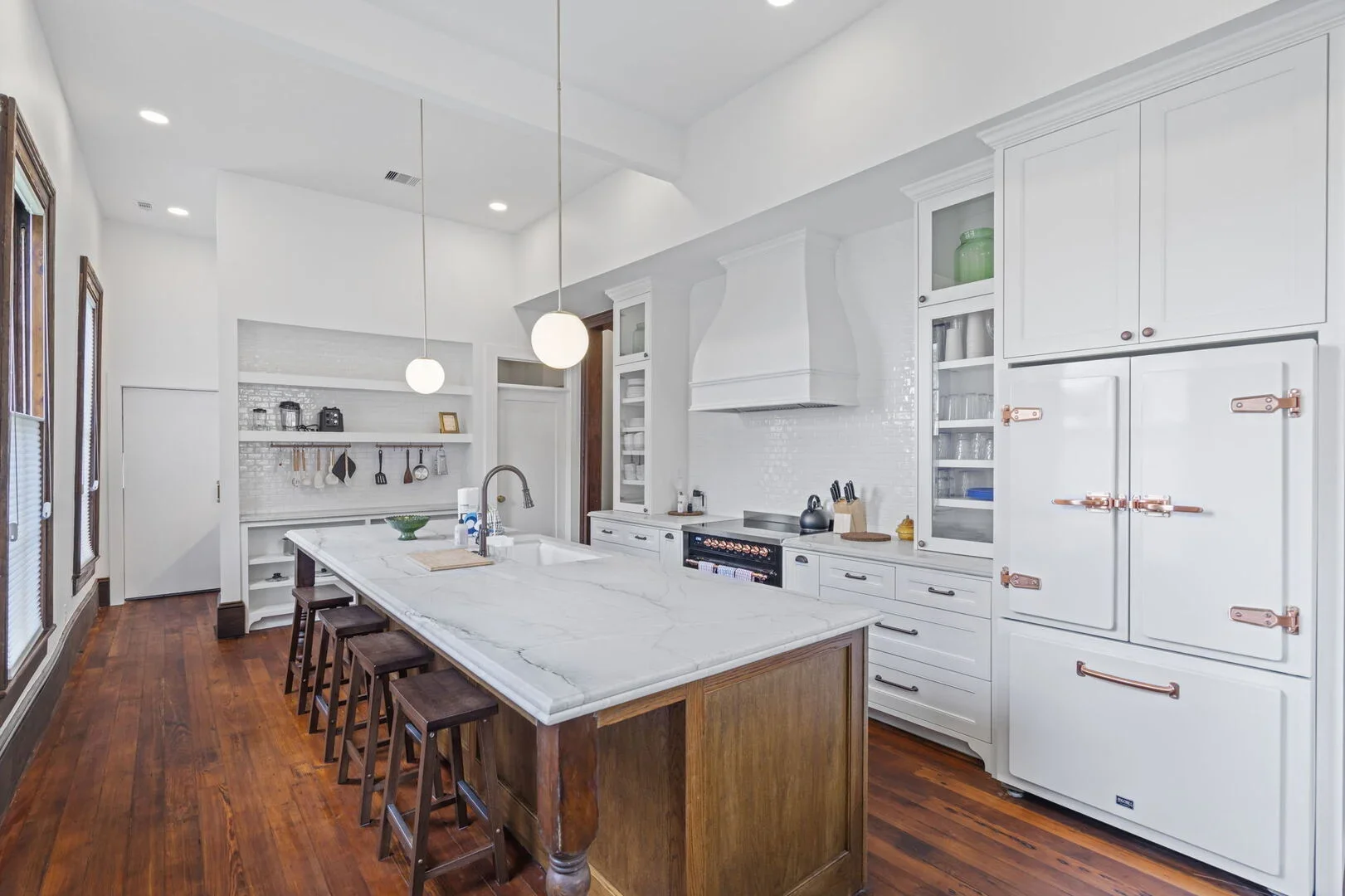 Mollie Walters House Kitchen modern kitchen with white cabinetry, a large marble island, wooden floors, and pendant lights.