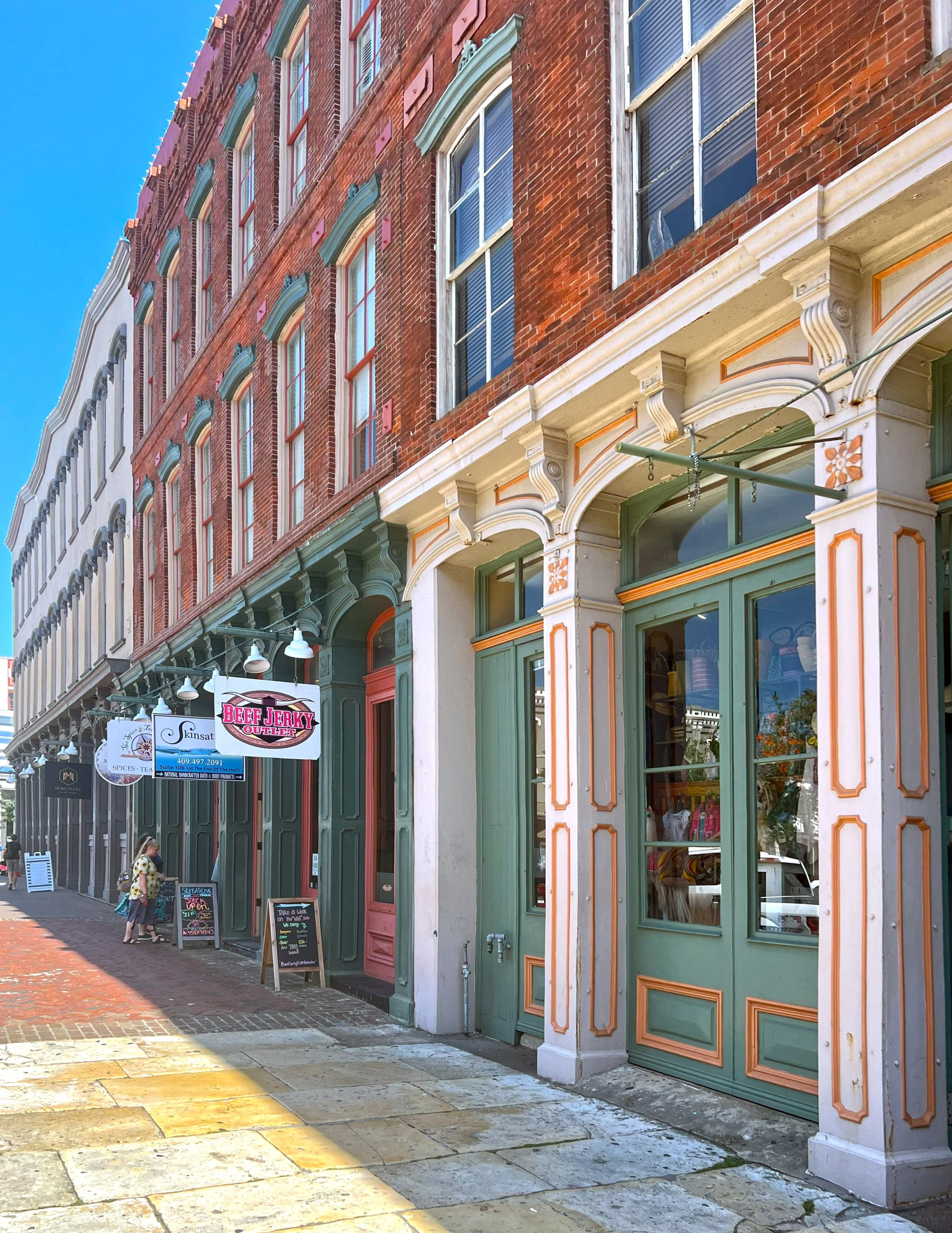 A row of historic storefronts with colorful decorative woodwork and large windows on The Strand in Galveston.