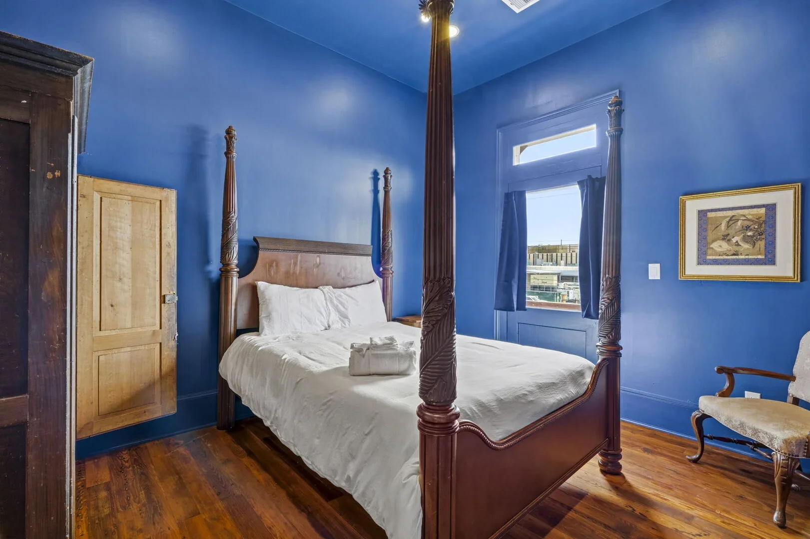 The Mollie Walters Navy Chamber with a wooden four-poster bed queen size bed, a wooden closet, a framed picture on the wall, and a vintage armchair.