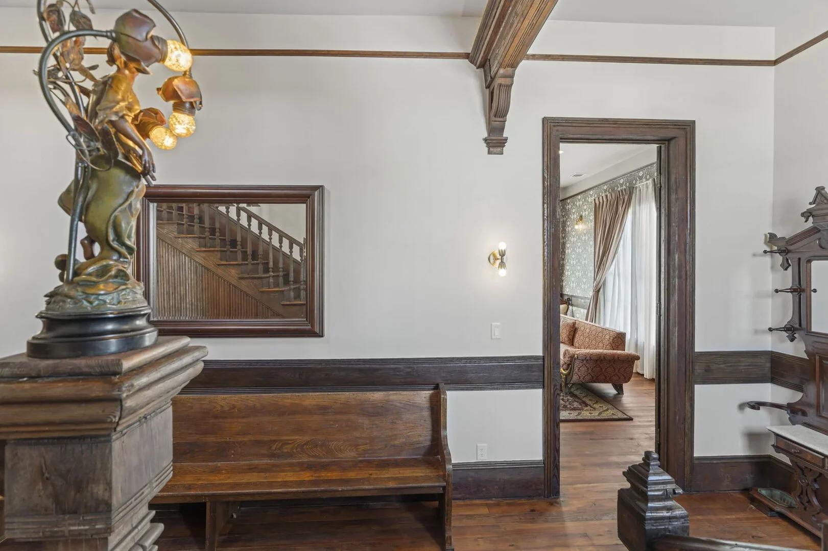 Interior of a Mollie Walters House with wooden trims, a mirror, a bench, a sculpture, and an open doorway leading to the Scarlet Parlor
