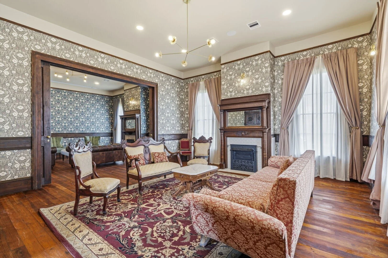 Mollie Walters Scarlet Parlor with vintage furniture, floral wallpaper, hardwood floors, fireplace, and large windows