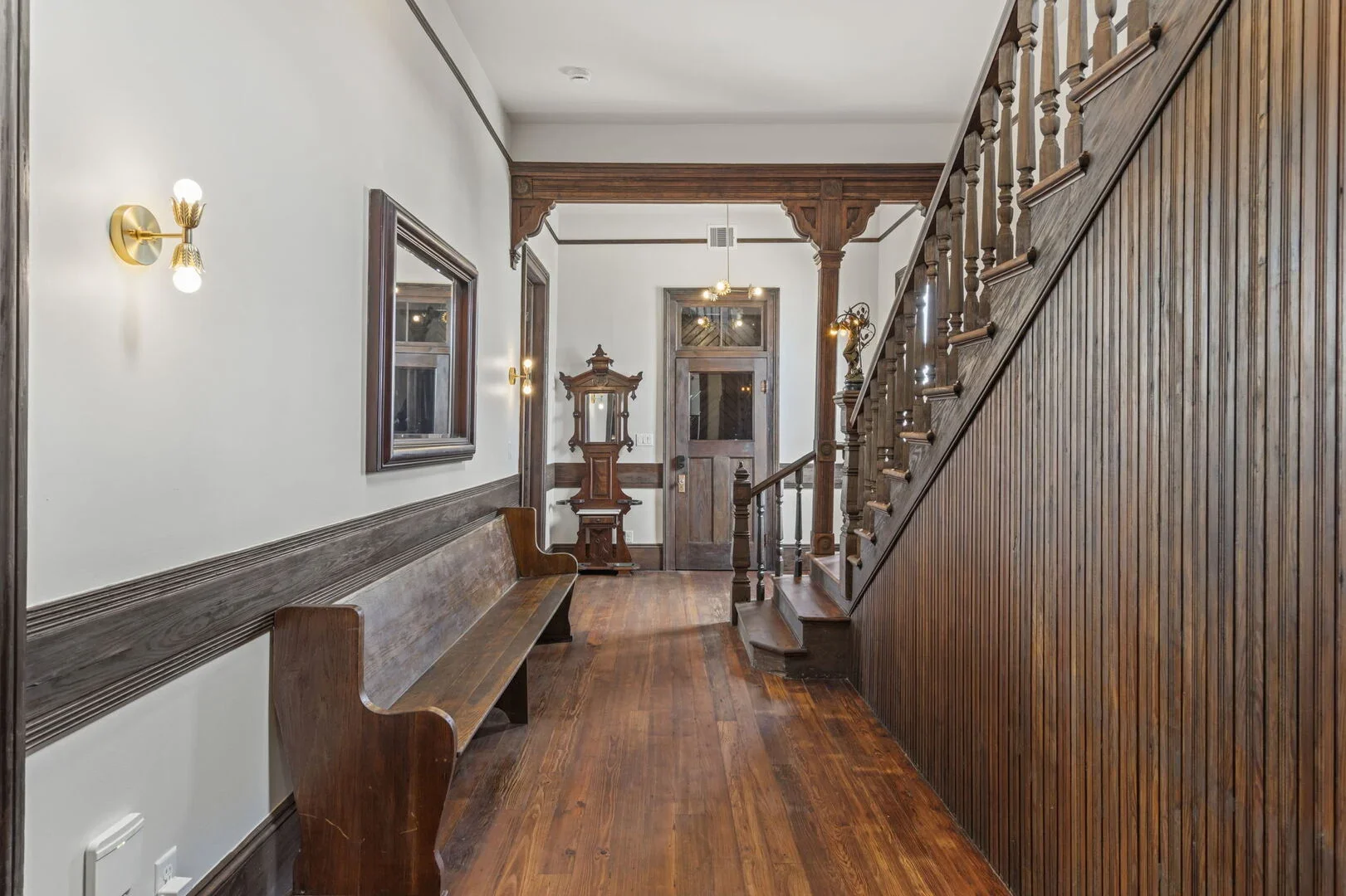 Mollie Walters House entryway with wood paneling, staircase, wooden bench, wall mirrors, and vintage coat rack.